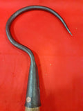 Garfio de hierro antiguo con mango de madera sobre fondo rojo, ideal para decoración rústica o coleccionismo. Pieza única de Cositas Antiguas.