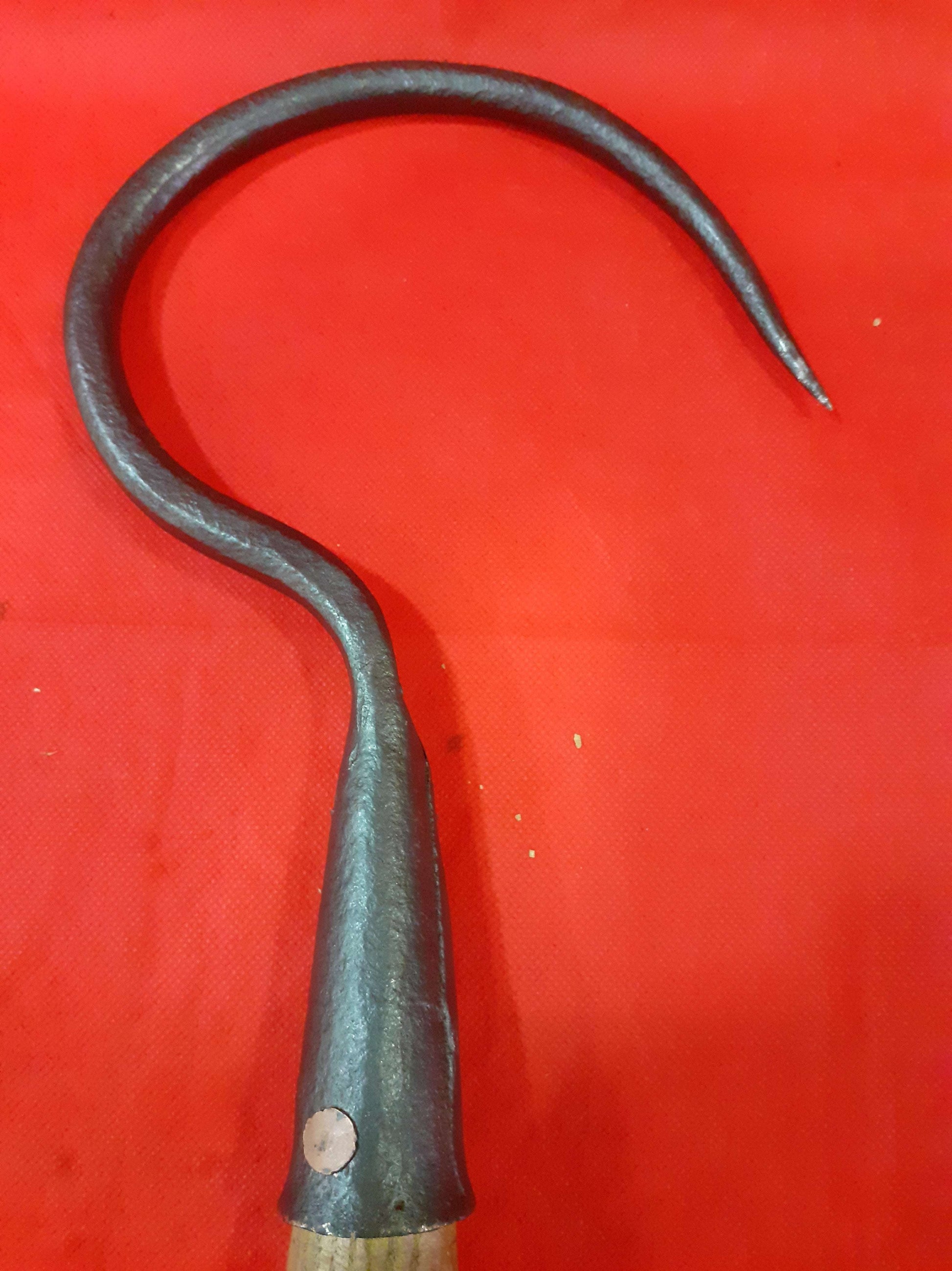 Garfio de hierro antiguo con mango de madera sobre fondo rojo, ideal para decoración rústica o coleccionismo. Pieza única de Cositas Antiguas.