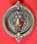 Aldaba antigua en forma de argolla con cabeza de león en bronce sobre fondo rojo. Ideal para decoración de puertas con estilo clásico y elegante.