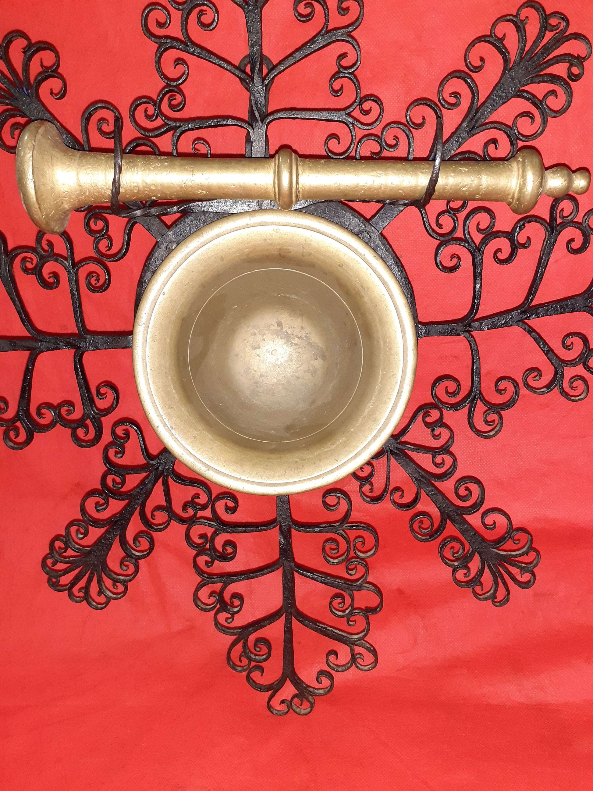 Mortero con filigranas antiguas en hierro forjado sobre fondo rojo, ideal como decoración de pared única para el hogar. Diseño artesanal exclusivo.