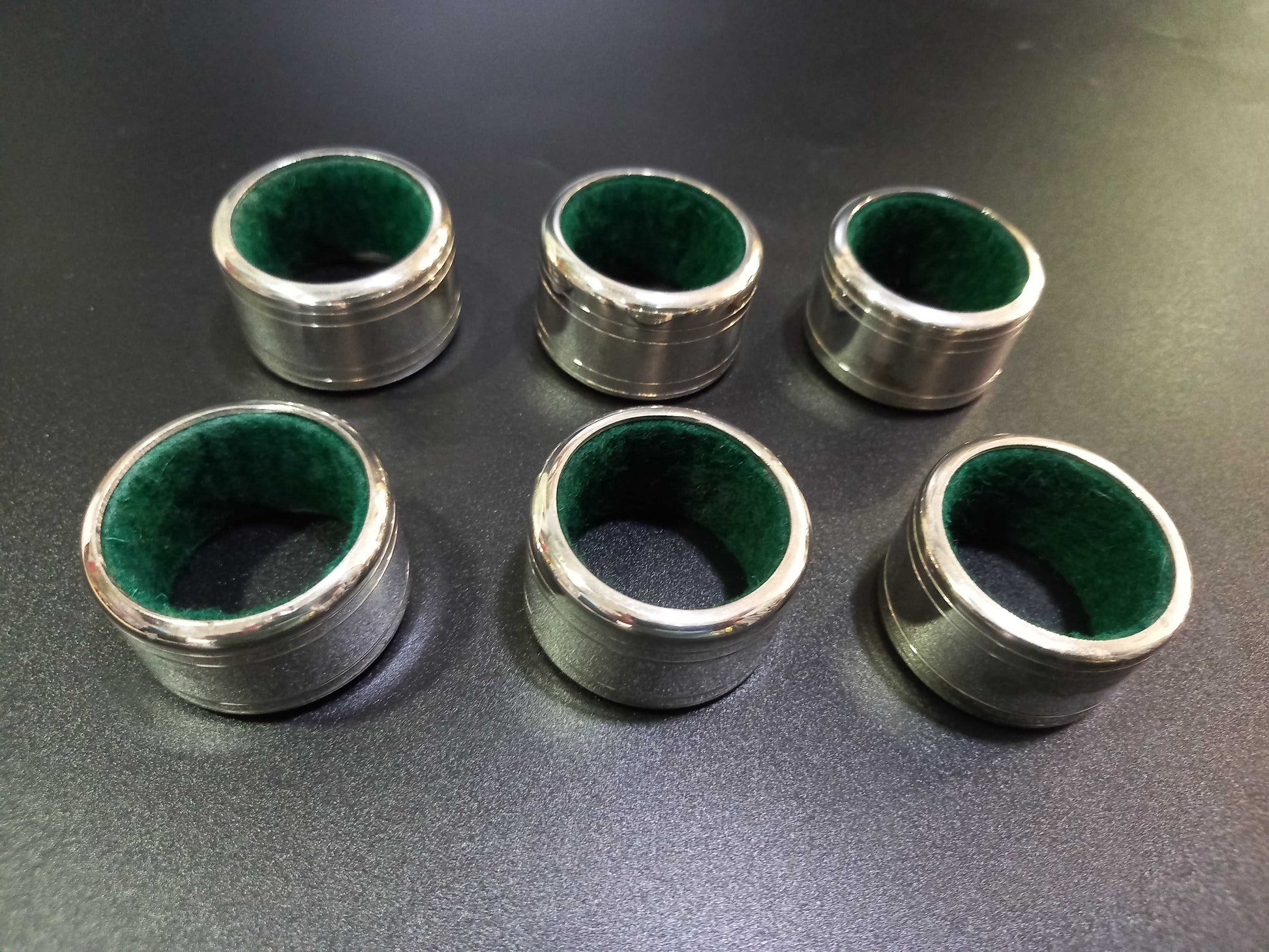 Set de 6 servilleteros de metal plateado con interior verde y números grabados, ideal para decoración de mesa elegante y clásica.
