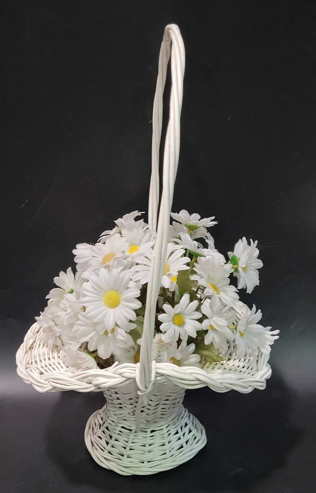 Canasto de mimbre blanco con margaritas blancas, estilo vintage ideal para decoración de interiores o eventos especiales en el hogar.