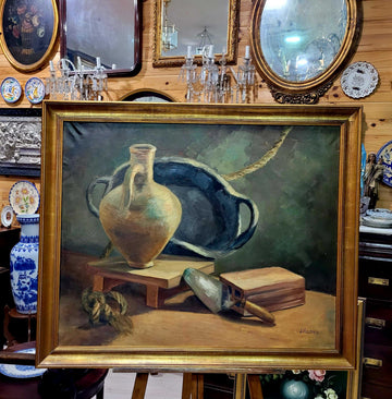 Óleo Bodegón con Marco Dorado Antiguo – Firma Lázaro exhibido en tienda de decoración, con jarrón, paleta y libro sobre fondo clásico.