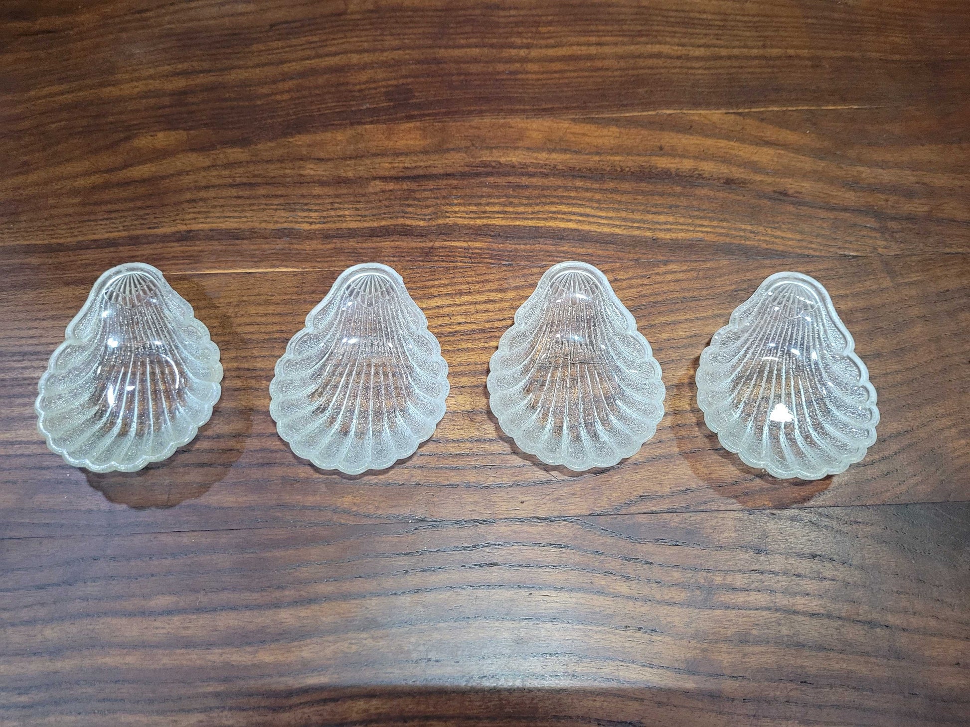 Cuatro conchas bautismales de cristal antiguo alineadas simétricamente, perfectas para decoración vintage en el hogar o eventos religiosos.