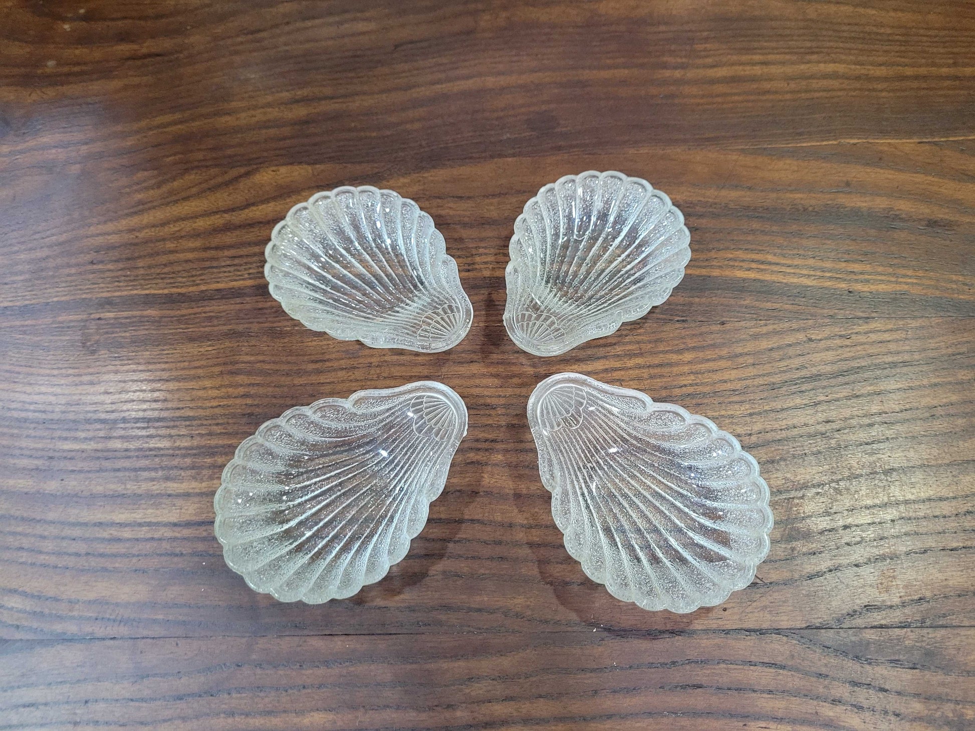 Conchas bautismales de cristal antiguas dispuestas en forma de cruz sobre superficie de madera, decoración elegante para ceremonias o colecciones.