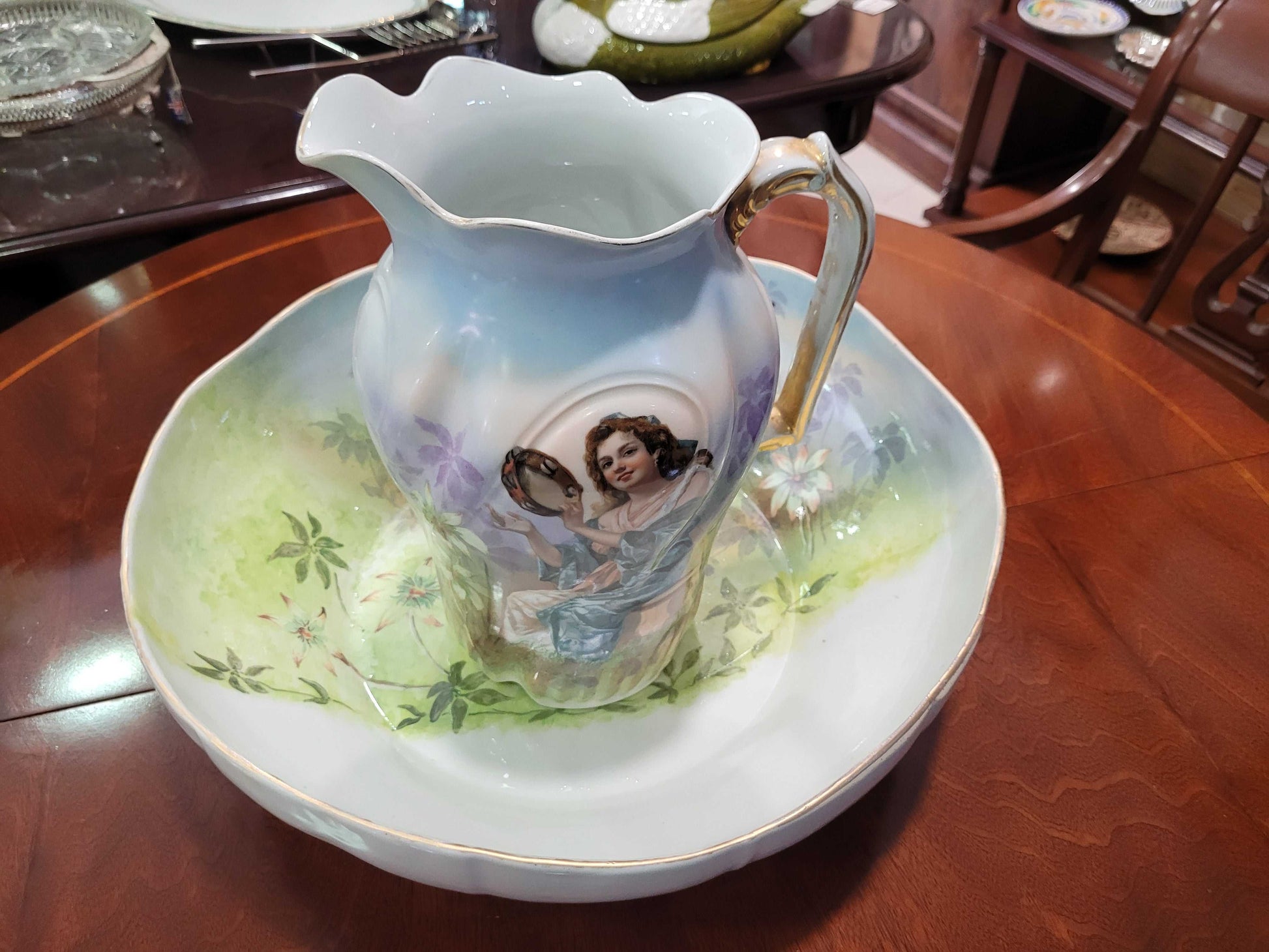 Jarra de porcelana Limoges del siglo XIX pintada a mano colocada sobre palangana a juego, ambas con motivos florales y figura femenina, pieza decorativa única.