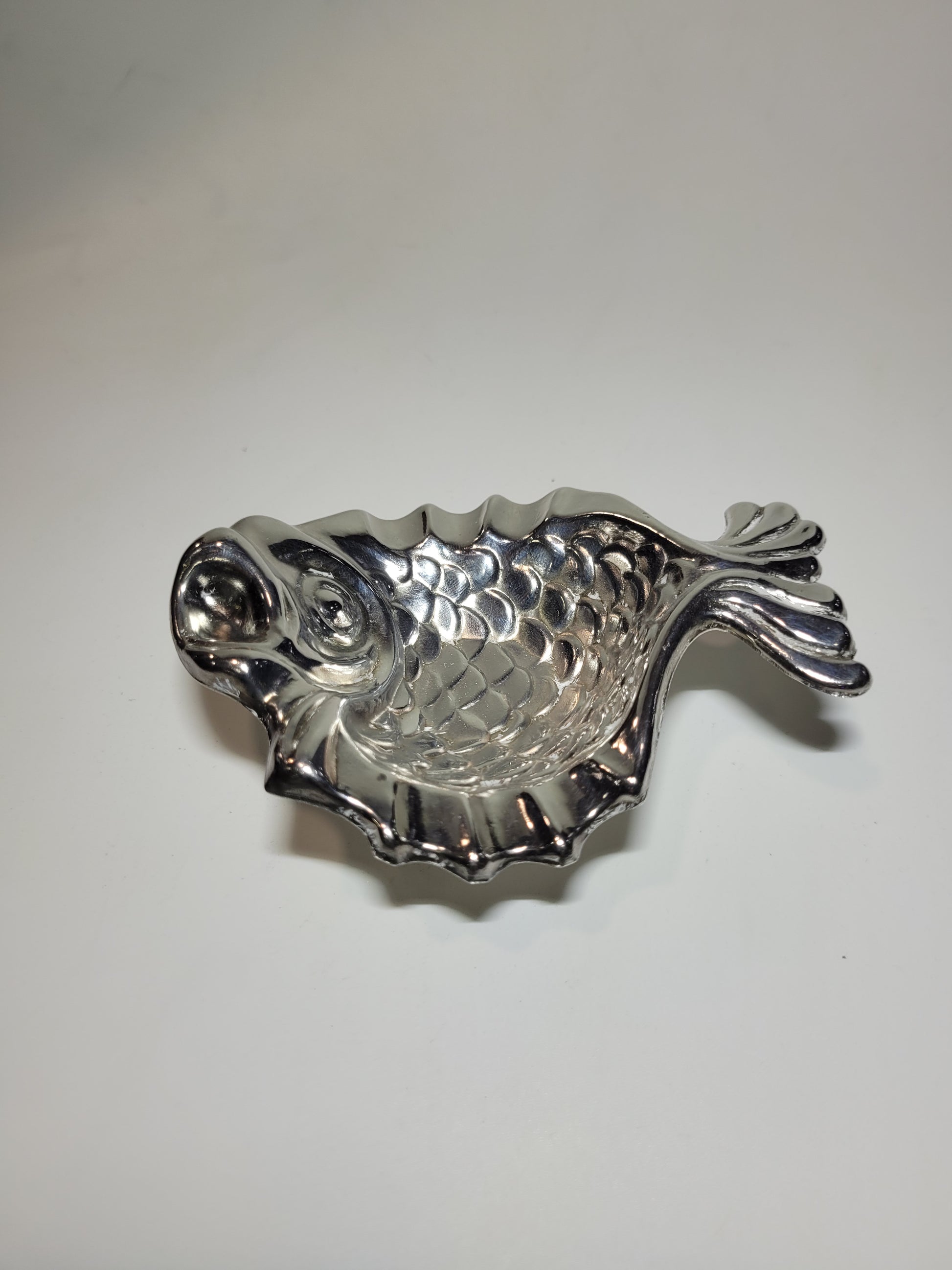 Cenicero vintage de metal plateado con forma de pez, diseño detallado y funcional para decoración en el hogar.