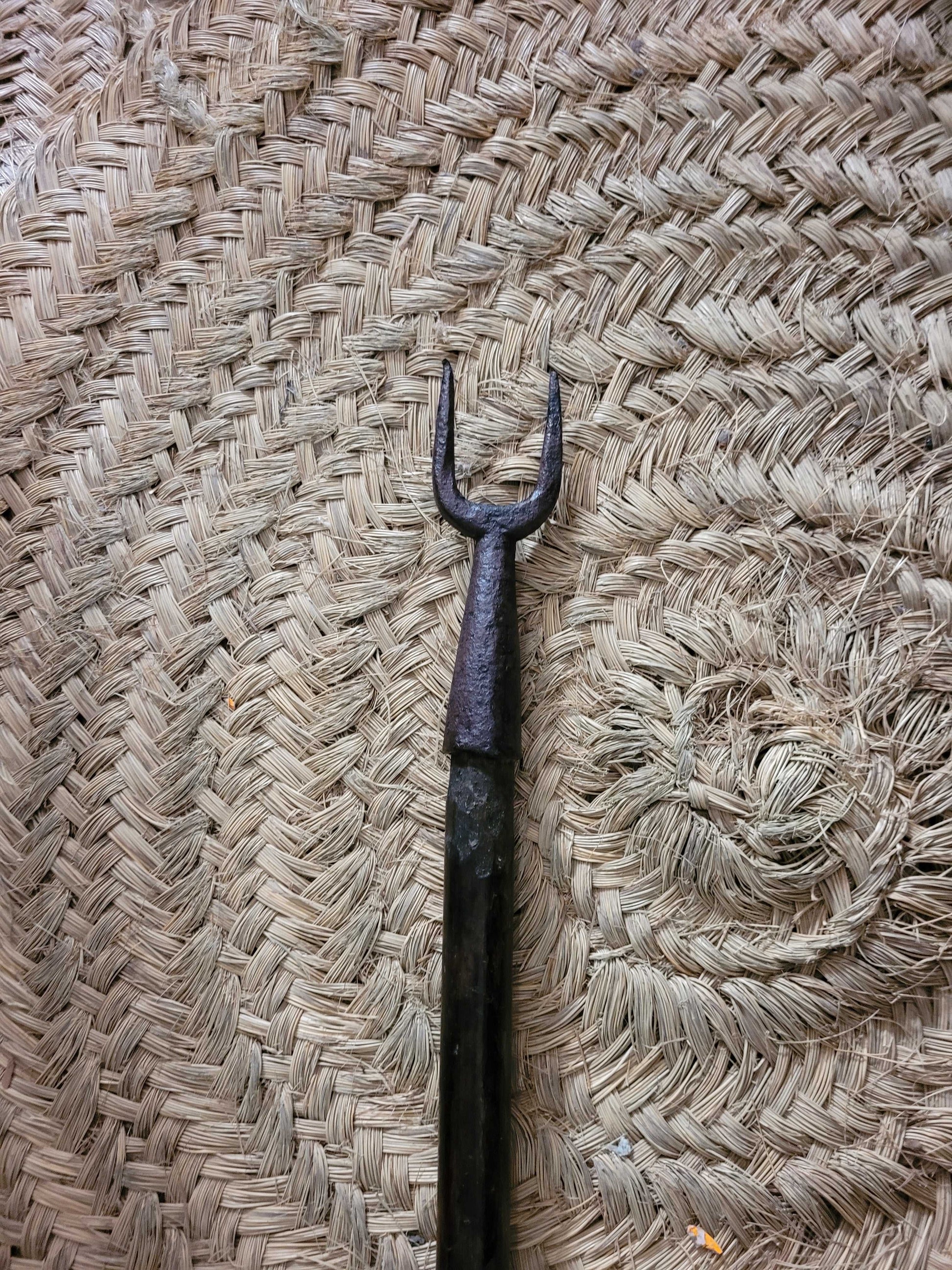 Horquilla antigua de hierro con largo palo de madera sobre suelo de piedra.