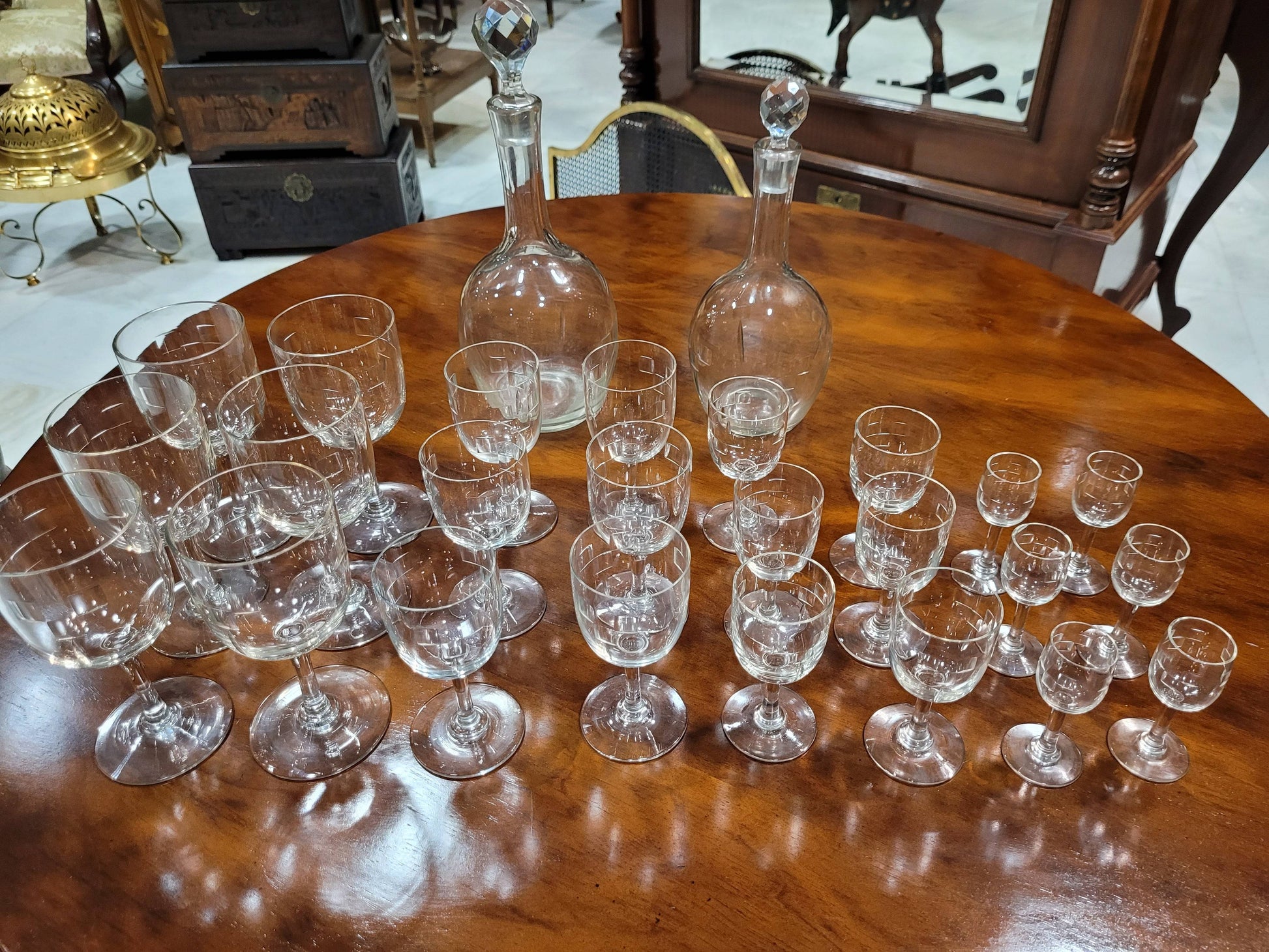 Cristalería antigua de diseño con 6 servicios completos, incluye copas de vino, agua, licor y dos licoreras sobre mesa de madera. Ideal para decoración de mesa elegante.