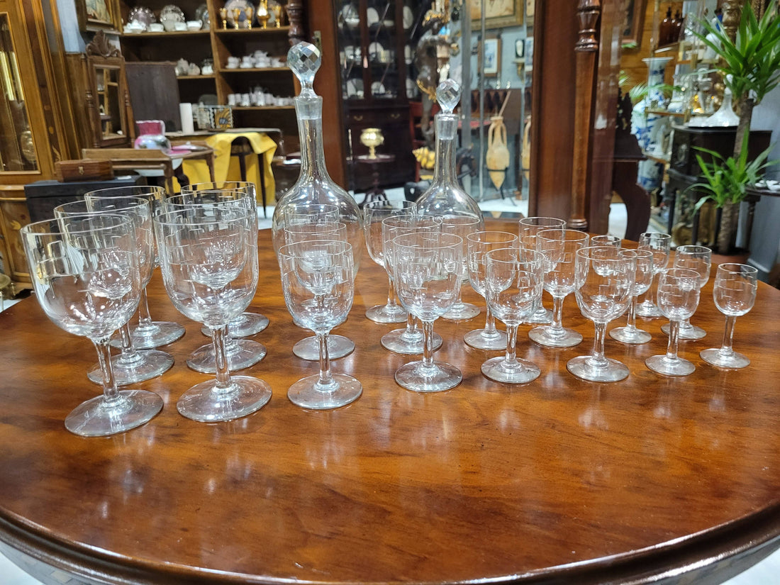 Cristalería antigua de diseño con 6 servicios completos, incluye copas de vino, agua, licor y dos licoreras sobre mesa de madera. Ideal para decoración de mesa elegante.