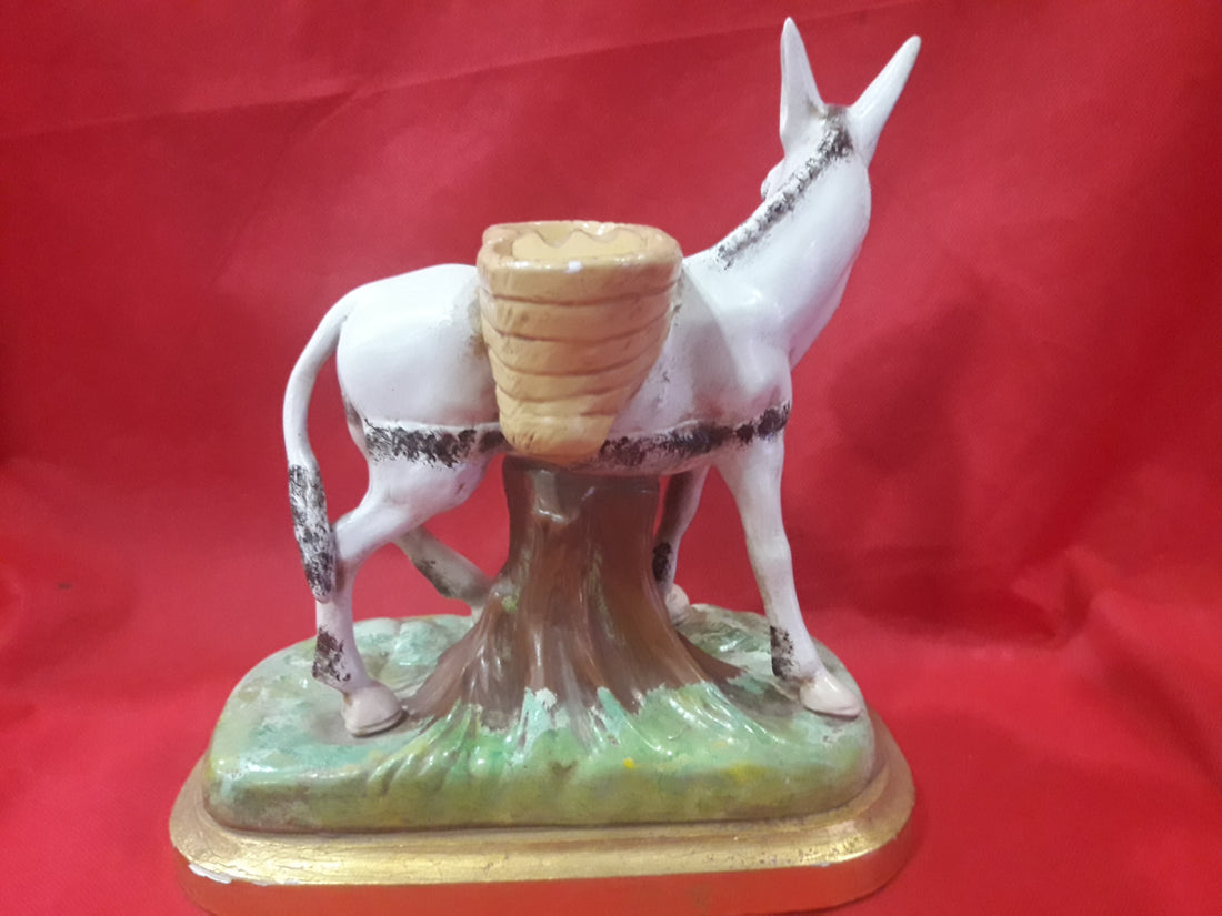 Figura de burro de porcelana con alforjas sobre base decorativa, ideal para decoración vintage. Disponible en Cositas Antiguas.