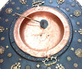 Brasero de cobre vintage con asas metálicas sobre mesa decorativa del siglo XVIII, ideal para decoración de interiores clásicos.