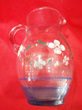 Jarra de cristal antigua decorada a mano con flores blancas sobre fondo rojo. Ideal para decoración vintage en el hogar con calidad y elegancia.