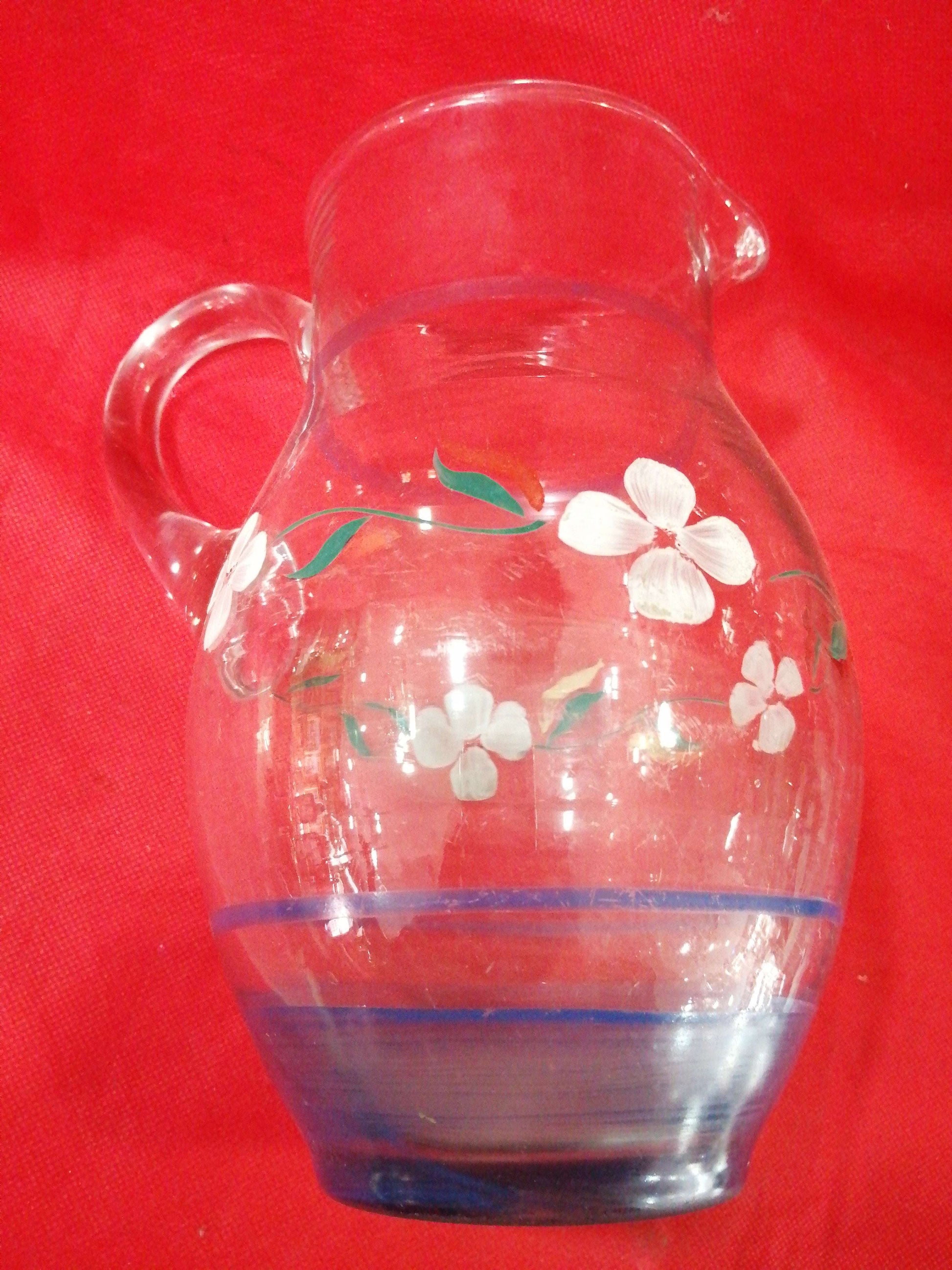 Jarra de cristal antigua decorada a mano con flores blancas sobre fondo rojo. Ideal para decoración vintage en el hogar con calidad y elegancia.