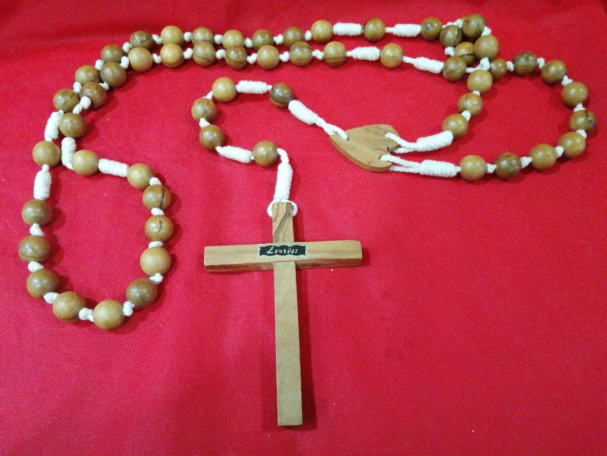 Rosario antiguo de madera con cuentas grandes y cruz tallada, ideal para decoración y oración. Diseño clásico sobre fondo rojo.