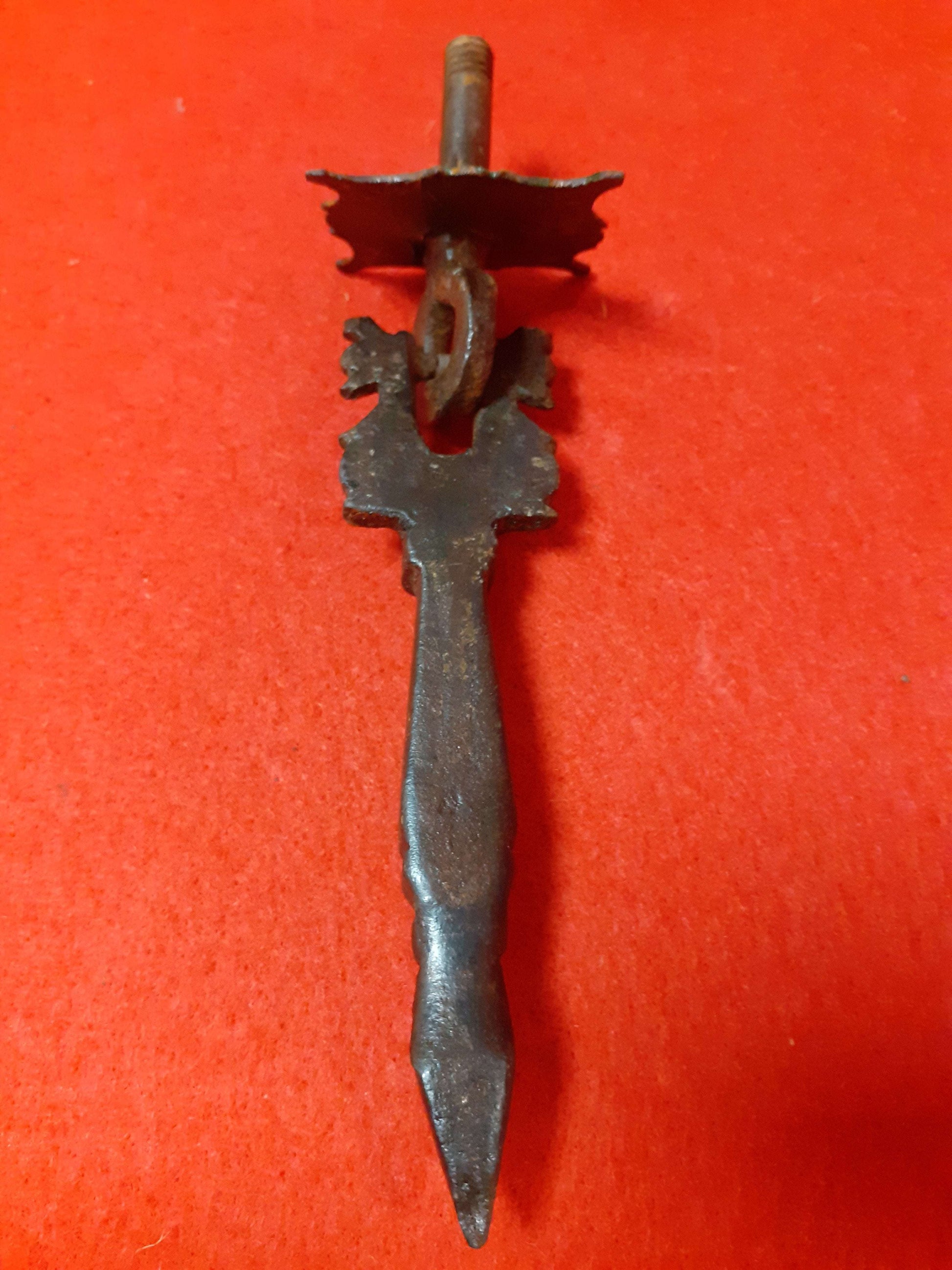 Aldaba Llamador de Puerta S. XVIII de hierro forjado sobre fondo rojo, diseño clásico con detalles ornamentales. Ideal para decoración de puertas rústicas.