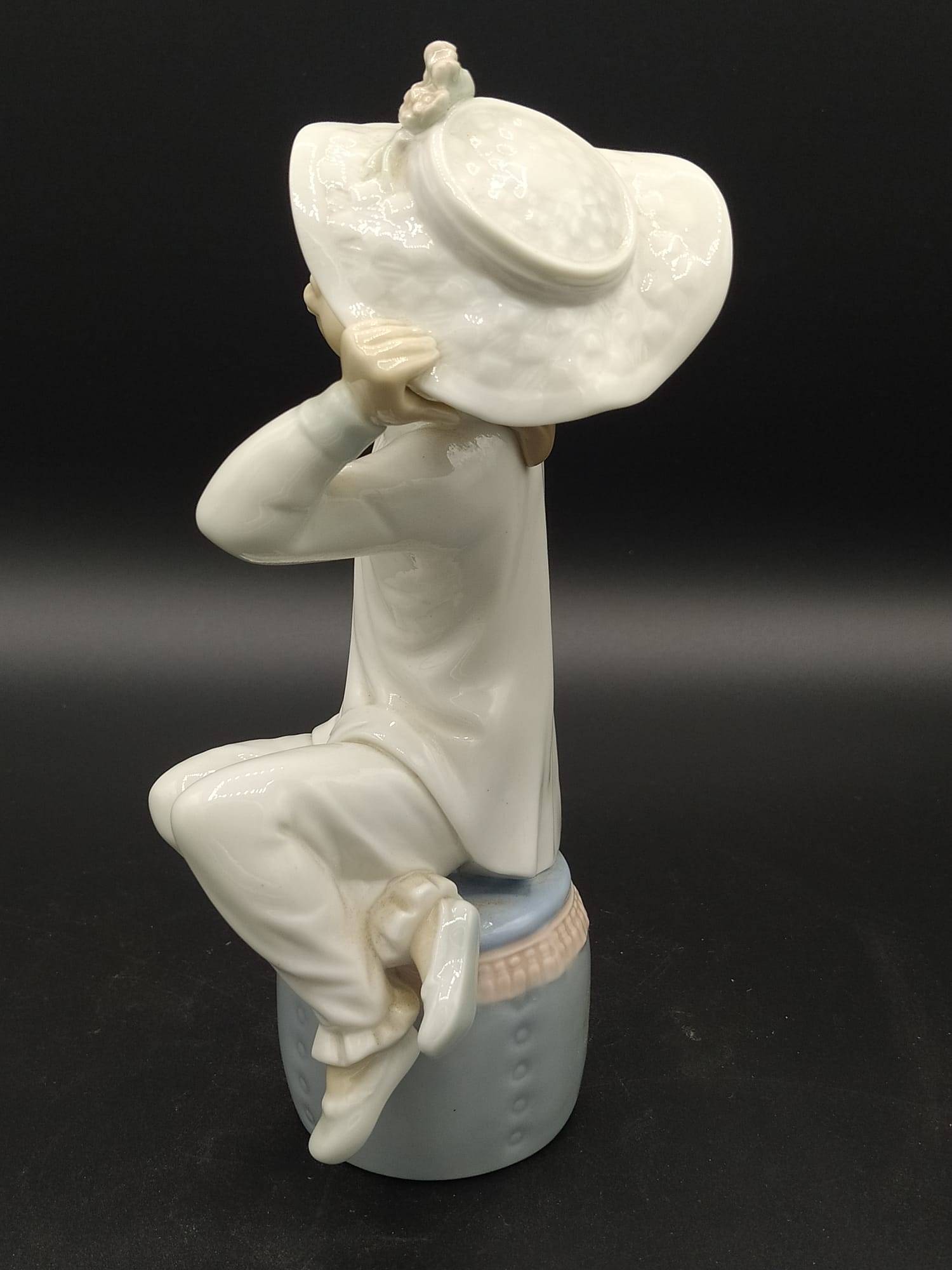 Vista trasera de la figura de porcelana Lladró 'Chica con gorro', destacando el sombrero con flores y la postura delicada sobre el tambor azul.