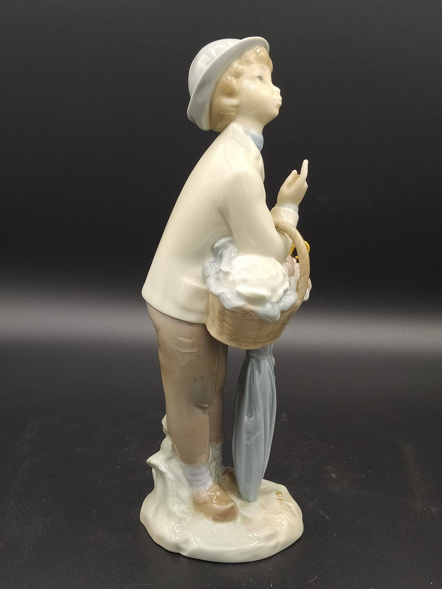 Figura Lladro Pequeño Jardinero de porcelana, vista lateral mostrando cesta de flores y paraguas, pieza decorativa vintage para hogar y jardín.