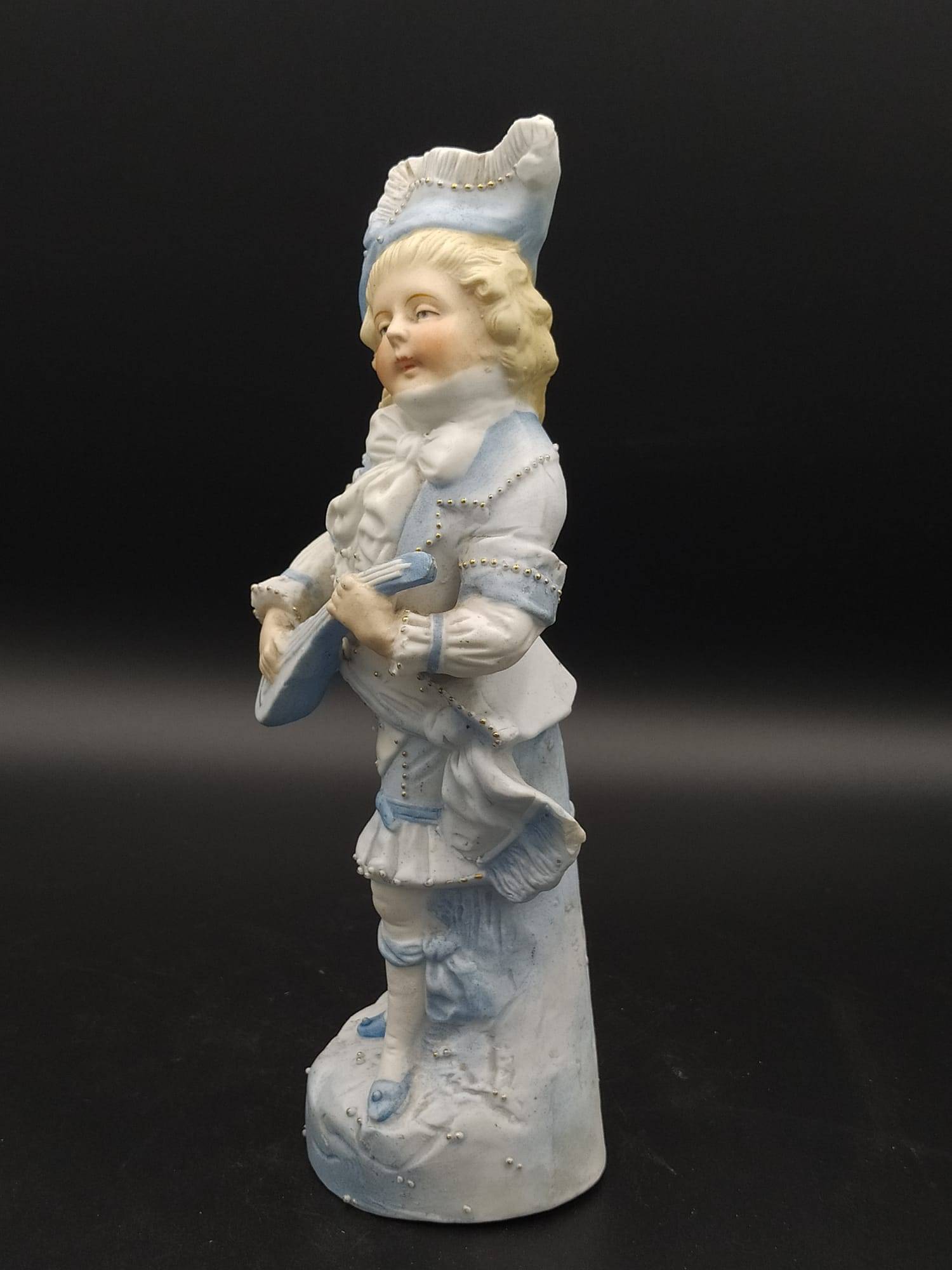 Decoración vintage: figura de porcelana antigua de galleta, niño músico con instrumento de cuerda y detalles en azul pastel.