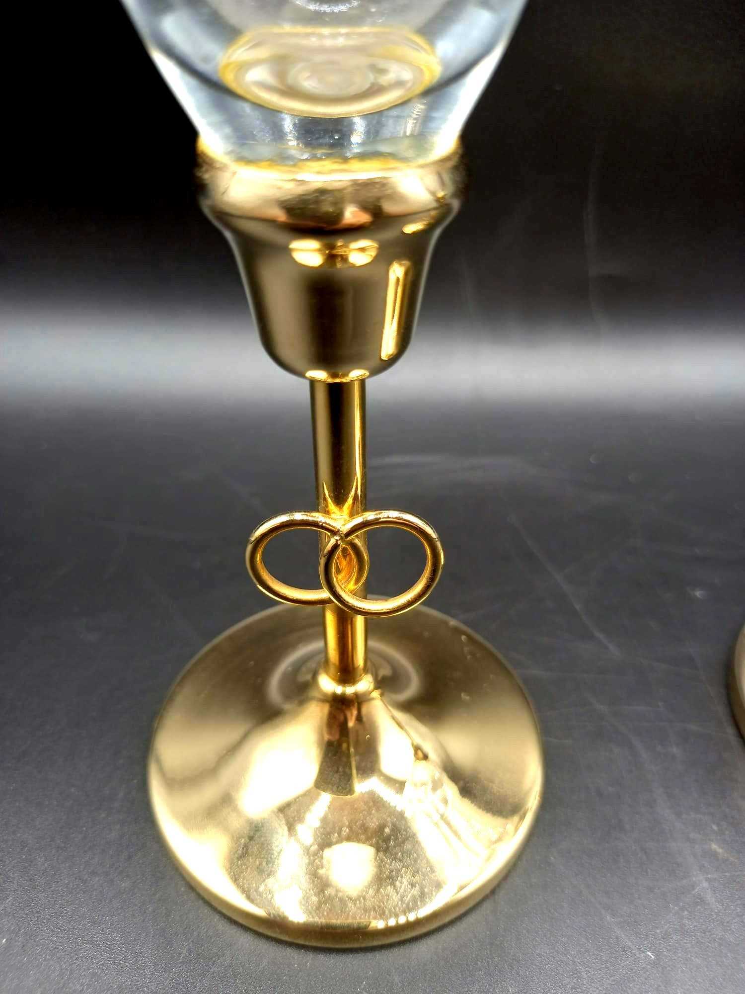 Detalle de copa de champán de cristal tallado con base dorada y anillos entrelazados, diseño elegante con oro de 24K para decoración de bodas.