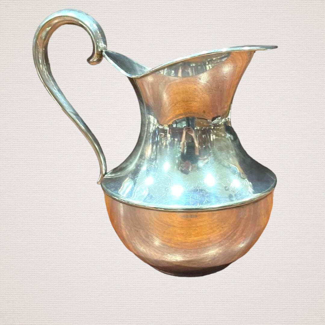 Jarra elegante de metal con asa curva y cuerpo pulido, versátil para uso funcional o como pieza decorativa en ambientes refinados.