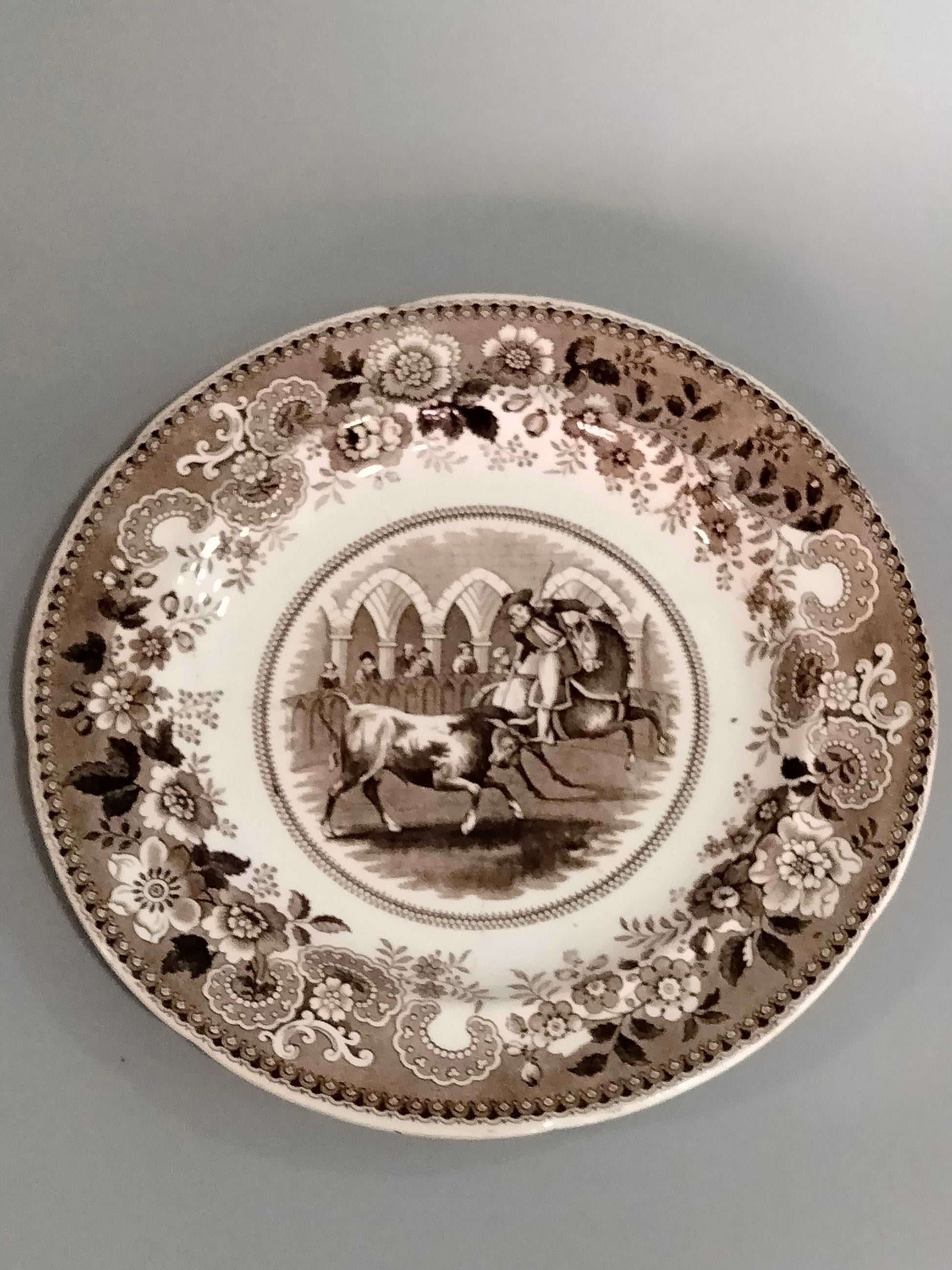 Plato de porcelana francesa antigua con escena de rejoneo en tonos sepia y borde floral detallado. Ideal para decoración vintage de alta calidad.