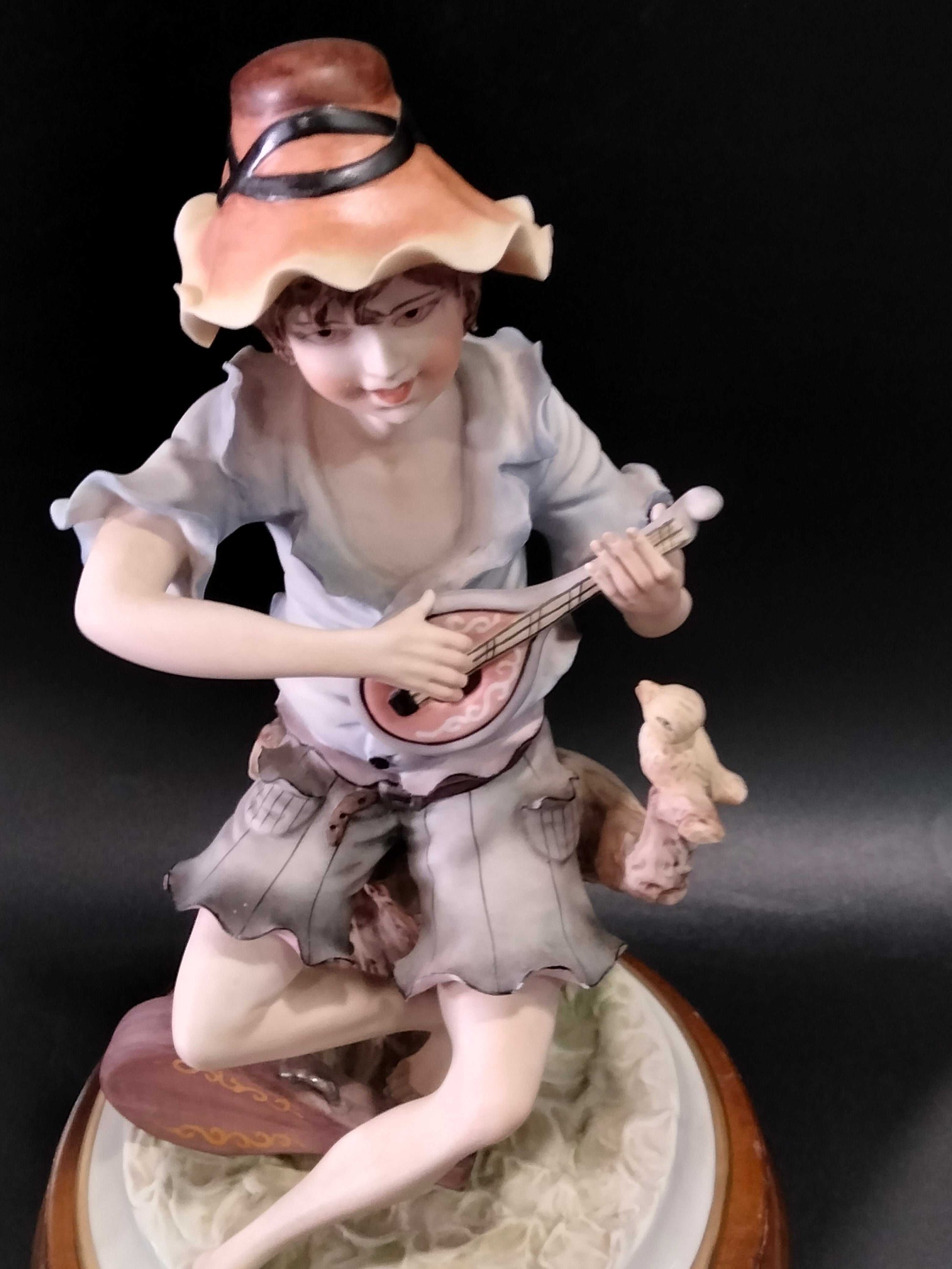 Figura de porcelana Carlos de niño tocando instrumento con pájaro en rama, diseño artístico y realista para decoración de hogar.