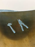 Detalle cercano del jarrón de metal con recortes artesanales de un martillo y un alicate, estilo único y vintage.