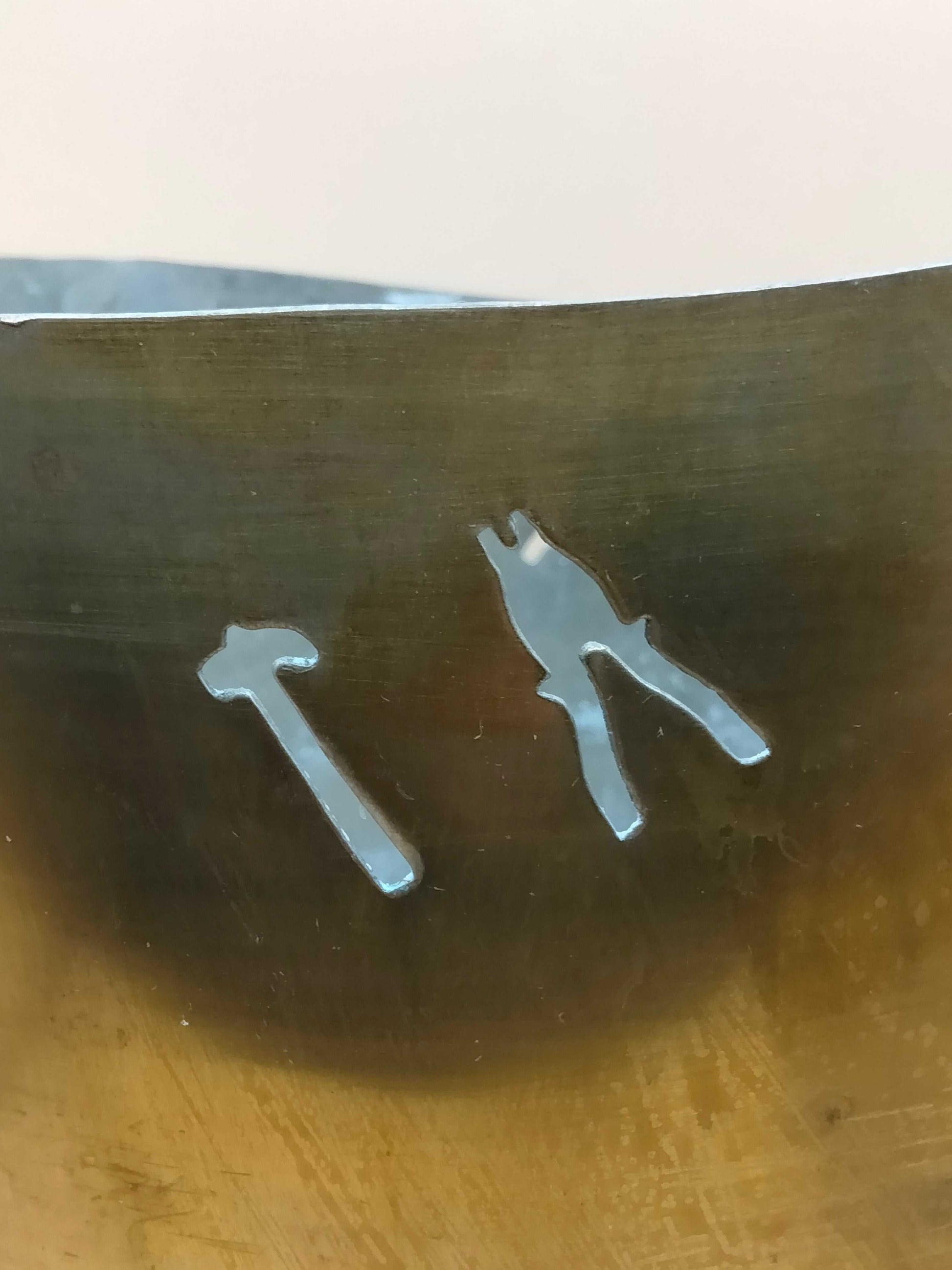 Detalle cercano del jarrón de metal con recortes artesanales de un martillo y un alicate, estilo único y vintage.