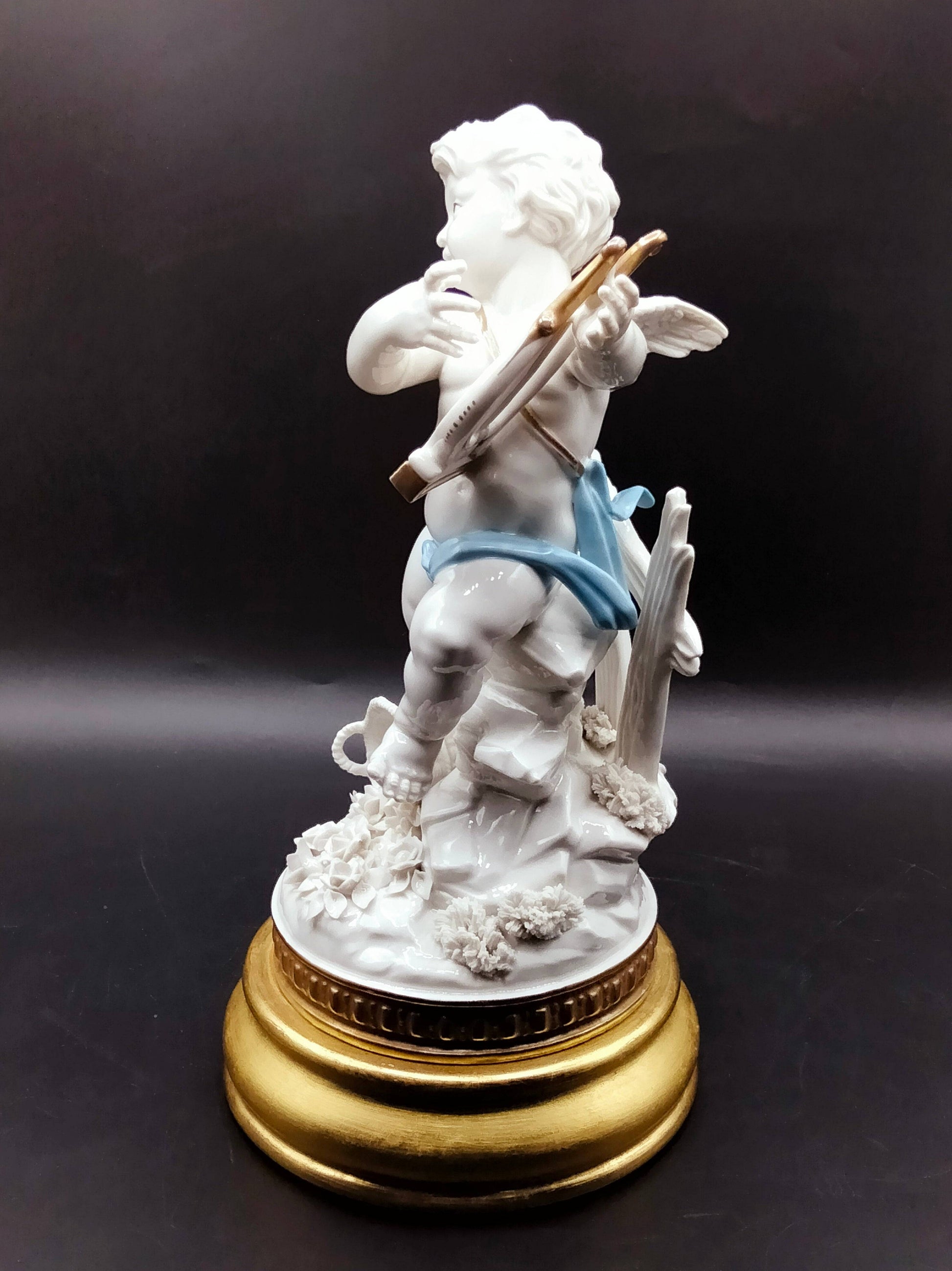 Angél Algora con arpa en porcelana fina, base dorada y detalles florales, pieza decorativa que transmite armonía y prosperidad.