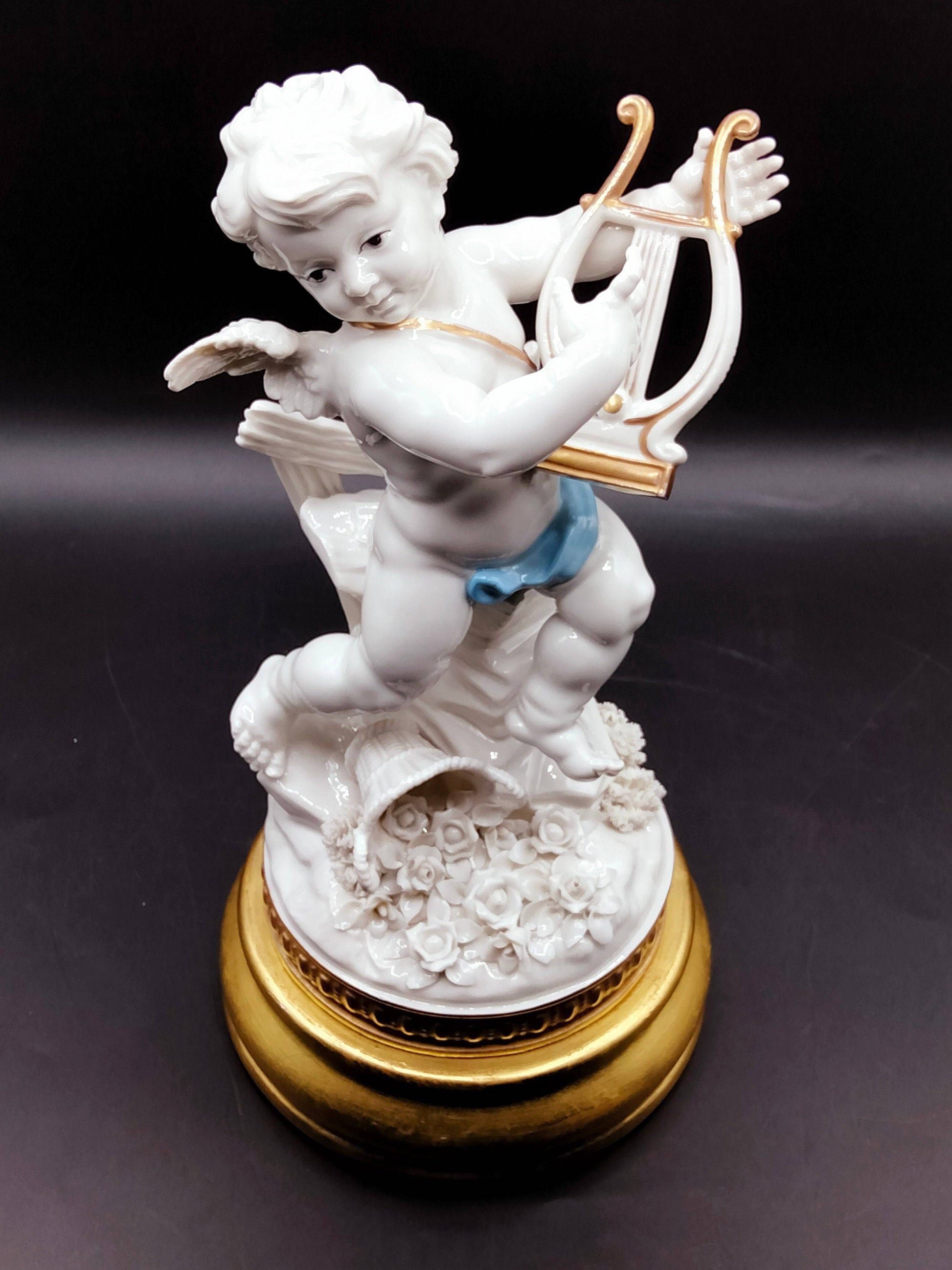 Escultura decorativa Angél Algora con arpa, acabado en porcelana blanca y azul, símbolo de suerte y belleza artesanal para el hogar.
