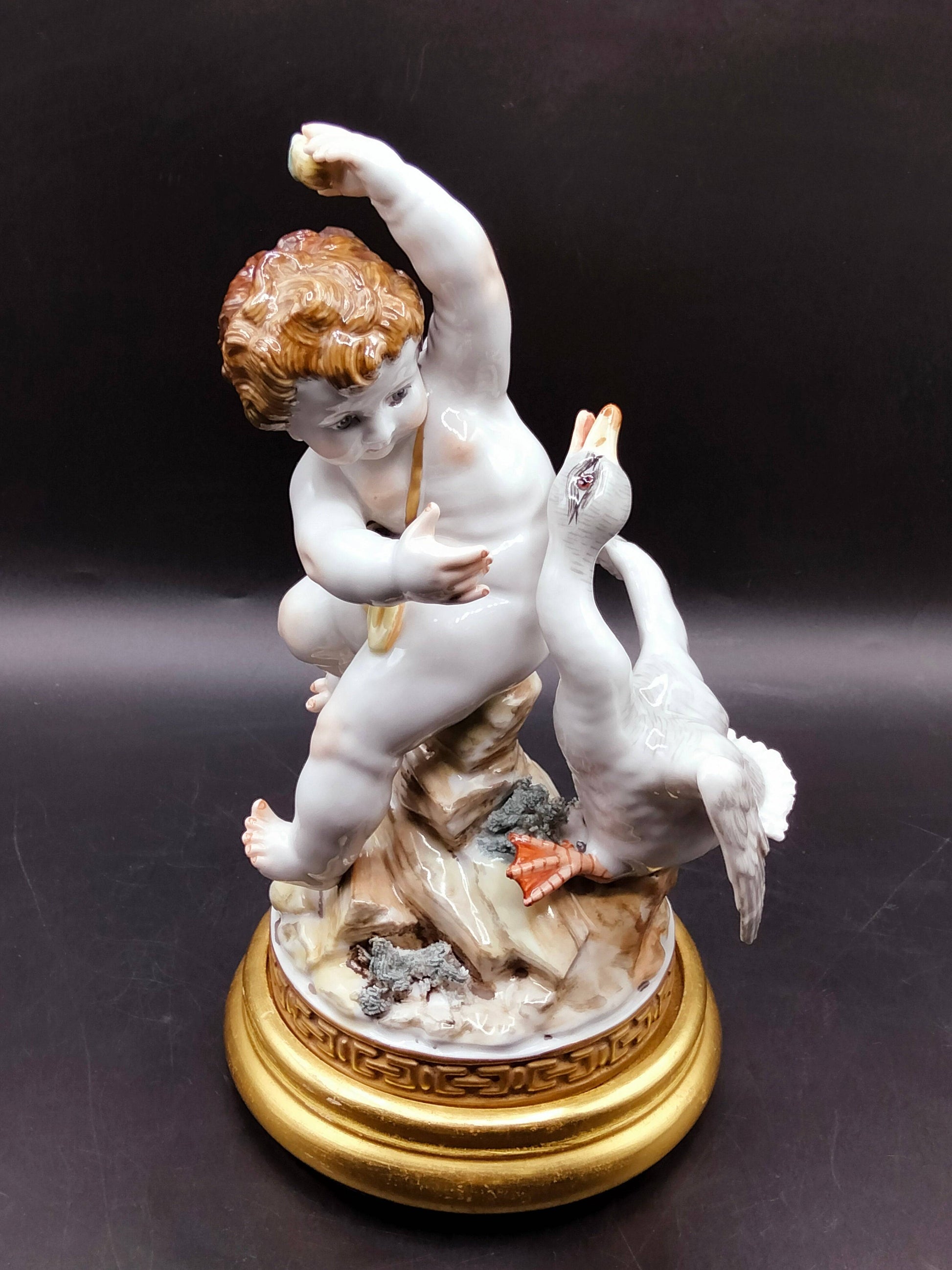 Figura decorativa Ángel con Pato de porcelana Algora, ángel infantil con expresión viva y pato en movimiento sobre peana dorada.
