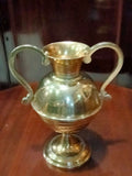 Ánfora antigua de bronce con diseño simétrico y base elevada, perfecta para decoración de hogar en estilo tradicional o rústico.