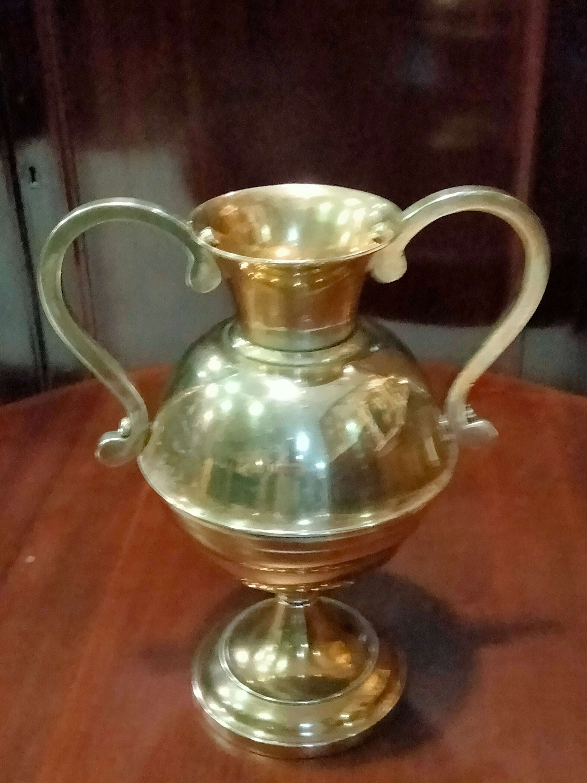 Ánfora antigua de bronce con diseño simétrico y base elevada, perfecta para decoración de hogar en estilo tradicional o rústico.
