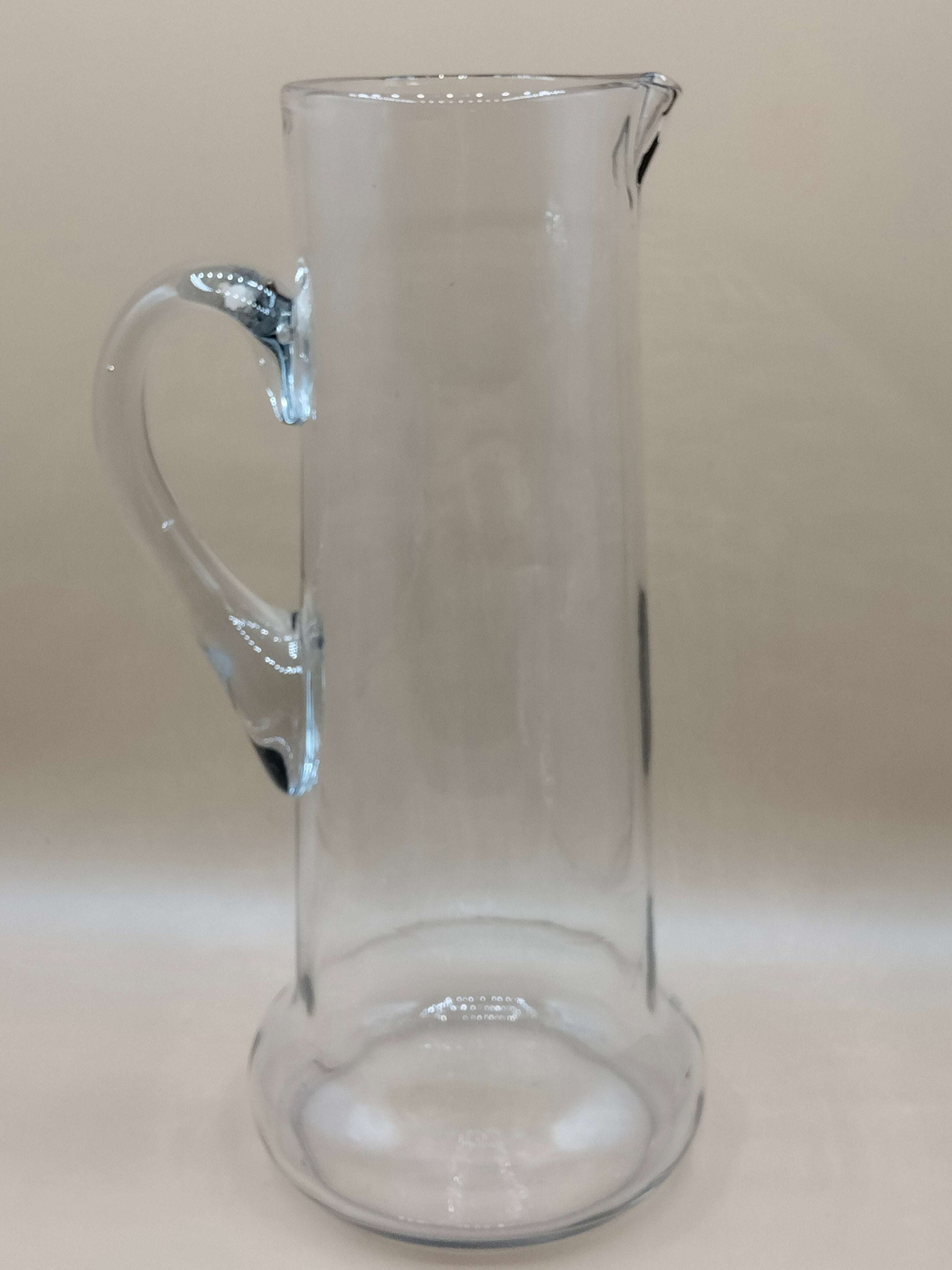 Jarra de cristal soplado del juego exclusivo de cristalería, con diseño artesanal y asa curva, ideal para servir agua con elegancia en la mesa.