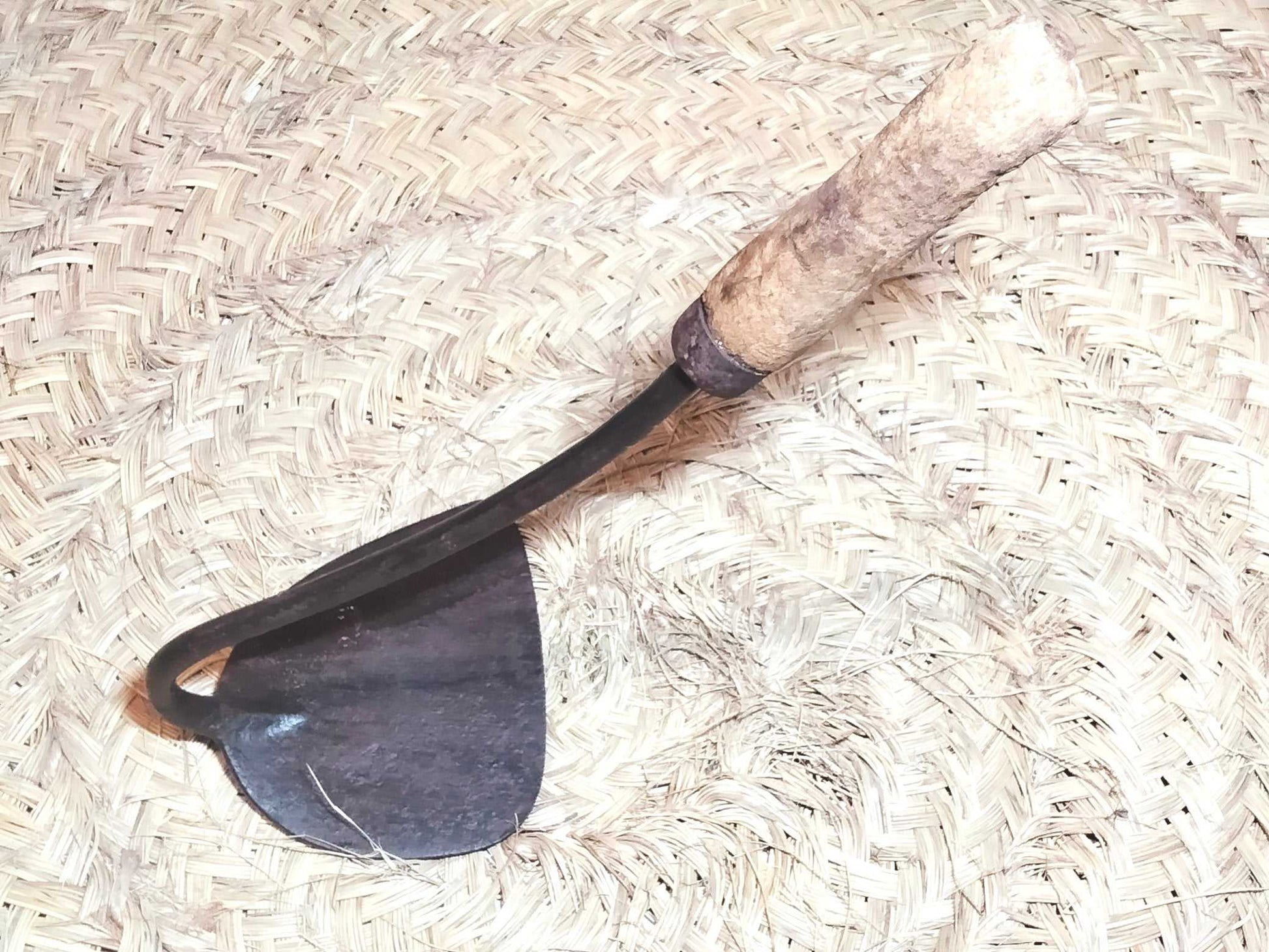 Herramienta de jardinería amocafre con hoja metálica y mango de madera, colocada sobre tapete artesanal. Diseño clásico para coleccionistas.