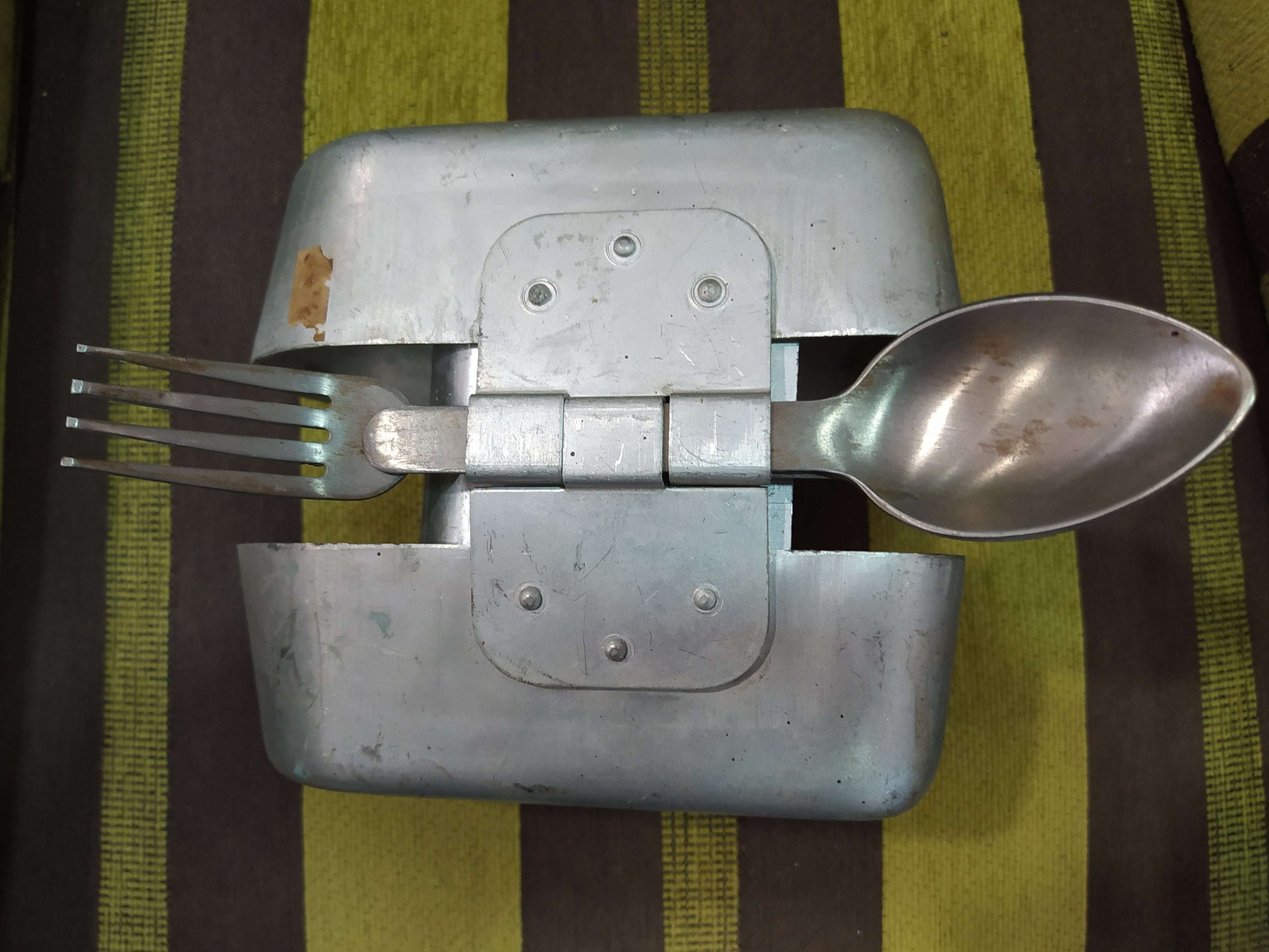 Fiambrera de aluminio antigua militar con cubiertos incluidos, ideal para decoración vintage en hogar o jardín. Diseño robusto y funcional.