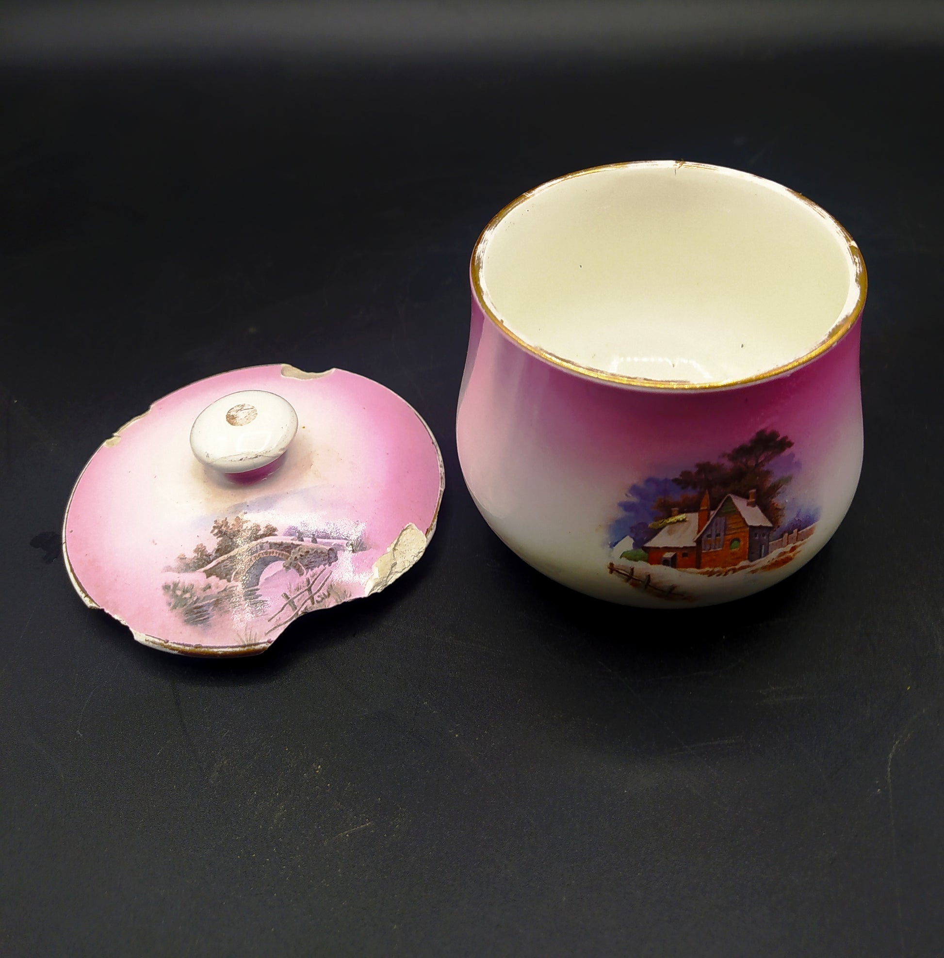 Tarro de tocador en porcelana Cartuja de Sevilla con tapa rota, diseño rosa con escena invernal. Ideal para decoración vintage de baño o tocador.