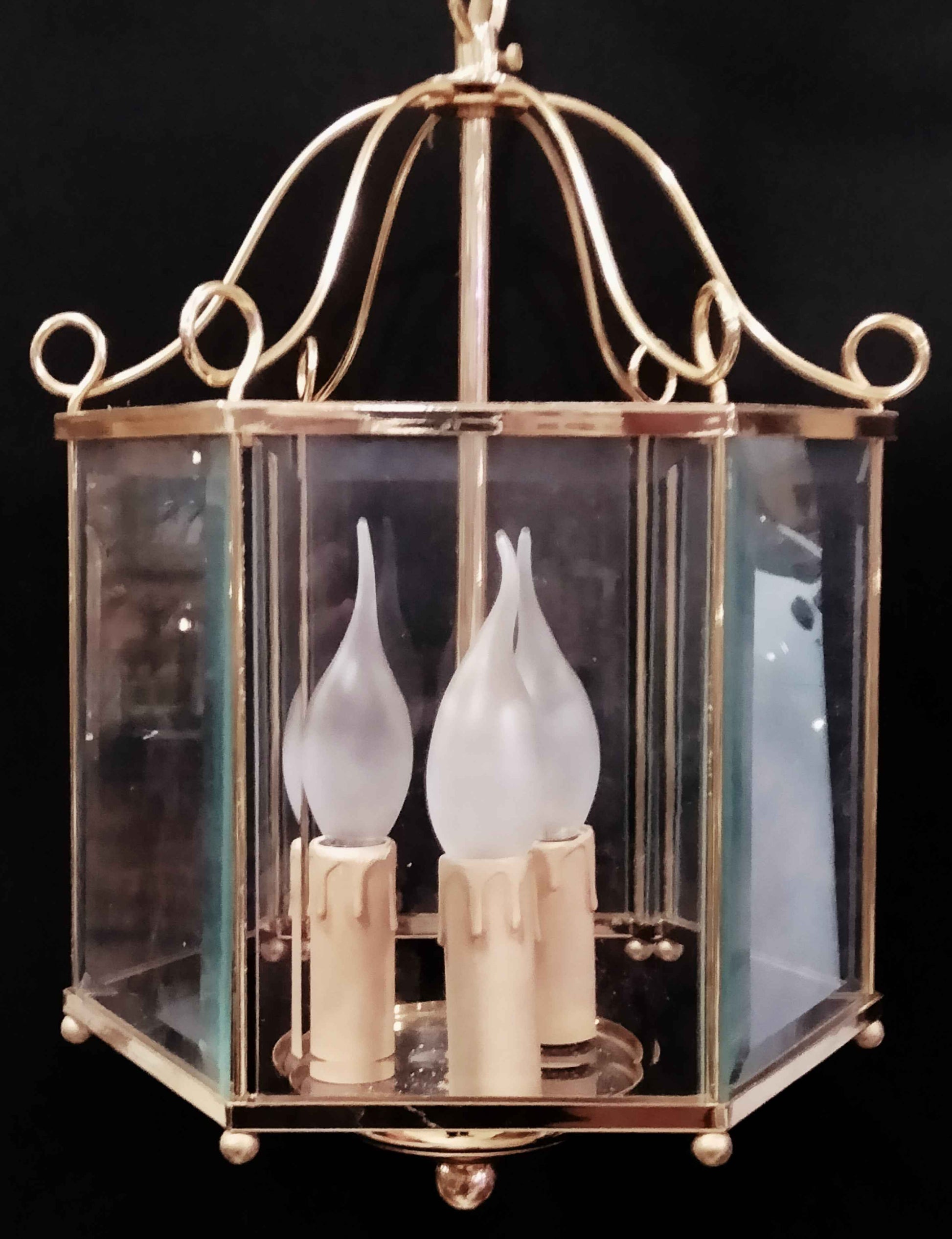 Detalle de lámpara farol de bronce dorado con cristales transparentes y bombillas en forma de llama. Perfecta para ambientes clásicos y sofisticados.