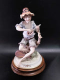 Figura de porcelana Carlos de niño con sombrero tocando instrumento de cuerda, sentado sobre base de madera, pieza decorativa de colección.