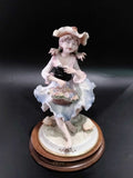 Figura de porcelana fina Carlos de niña con sombrero y vestido azul, sosteniendo canasta de flores, ideal para decoración de interiores.