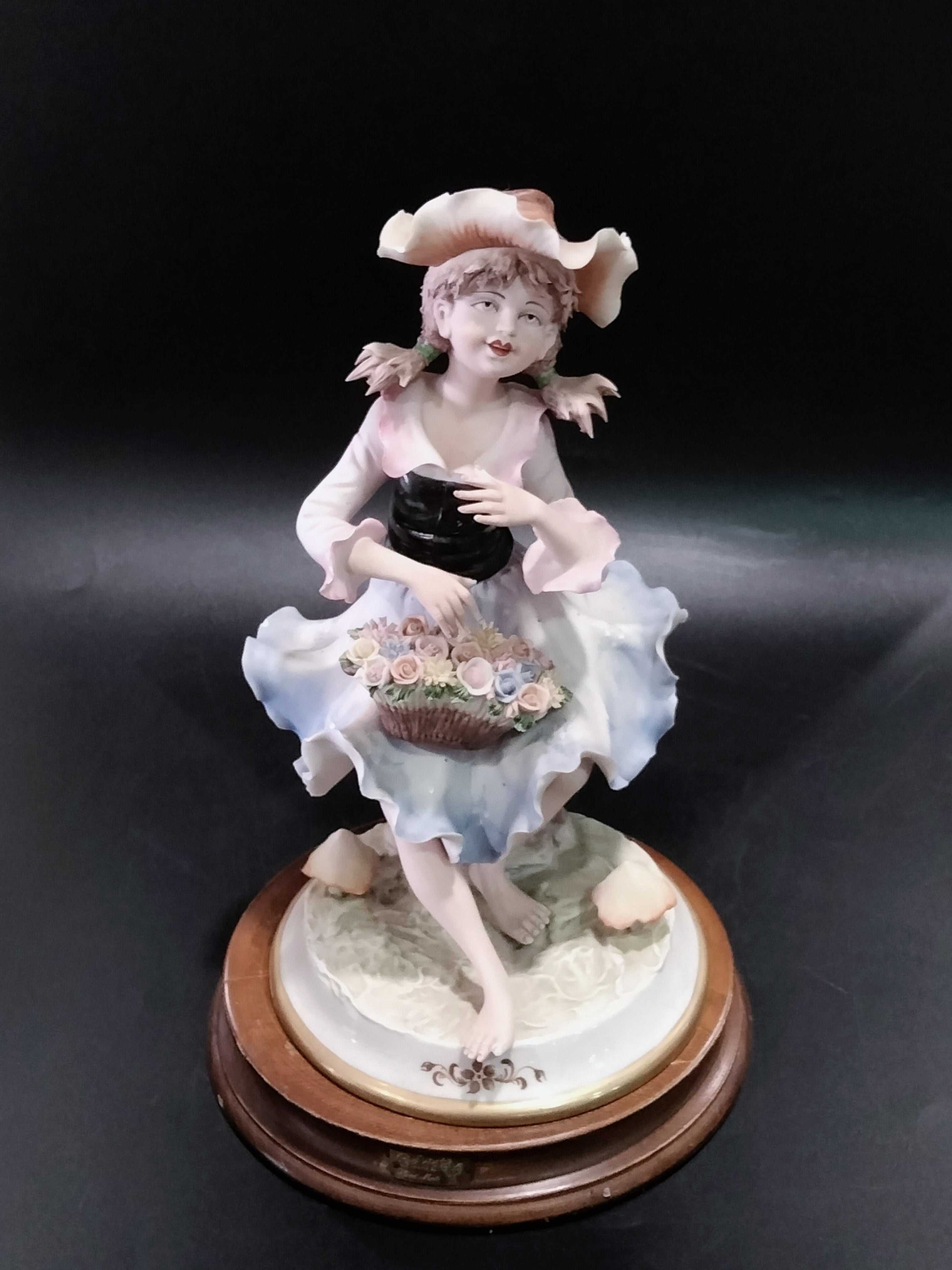 Figura de porcelana fina Carlos de niña con sombrero y vestido azul, sosteniendo canasta de flores, ideal para decoración de interiores.