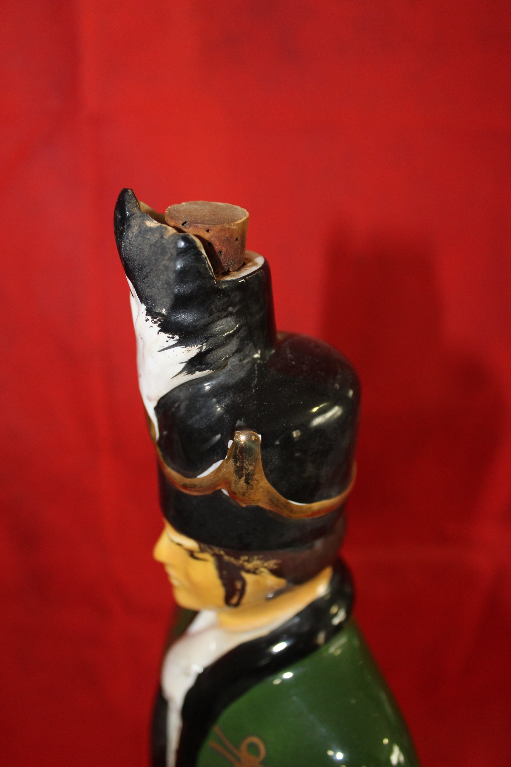 Figura de porcelana Iris Mist con forma de soldado de caballería, detalle del sombrero con tapón de corcho, fondo rojo.