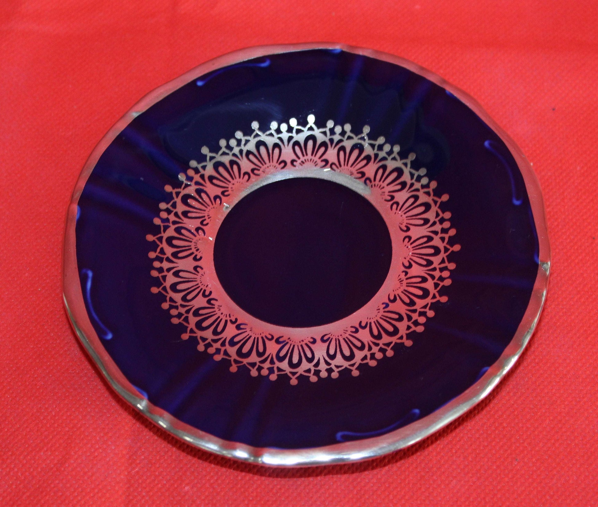 Plato de porcelana del Juego de Café Azul Cobalto con Hilo de Plata, decorado con elegante diseño clásico sobre fondo rojo. Ideal para decoración de mesa.