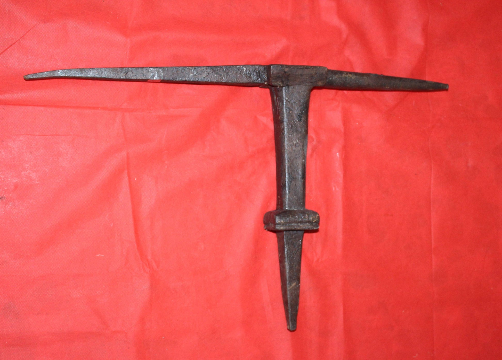 Yunque de latero en hierro forjado sobre fondo rojo, herramienta antigua para reparación de piezas de hojalata. Ideal para decoración vintage.