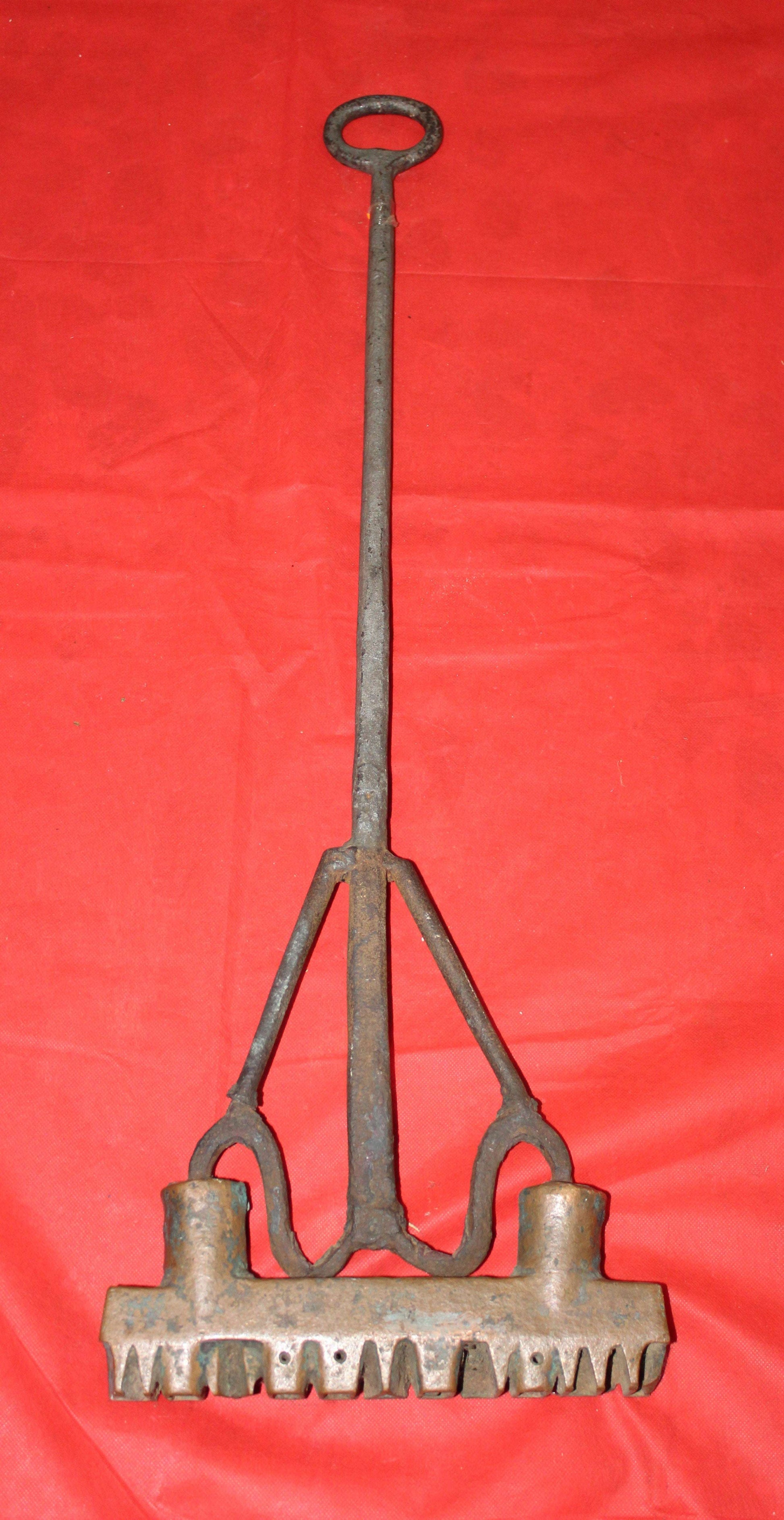 Hierro de marca J.Holgado y Cia para botas de vino en forja artesanal sobre fondo rojo. Decoración rústica ideal para coleccionistas de objetos antiguos.