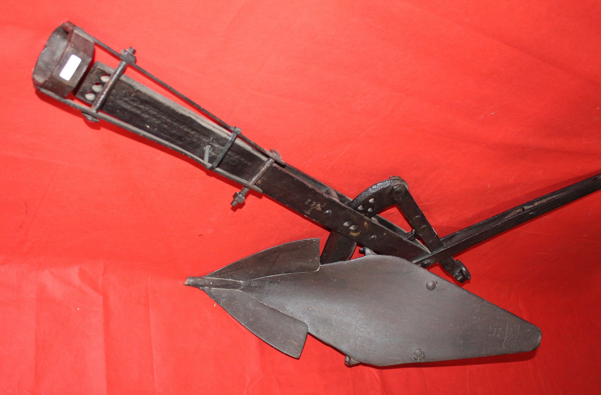 Antiguo arado de vertedera de tracción animal en hierro forjado sobre fondo rojo, pieza decorativa de excelente calidad para hogar o jardín.