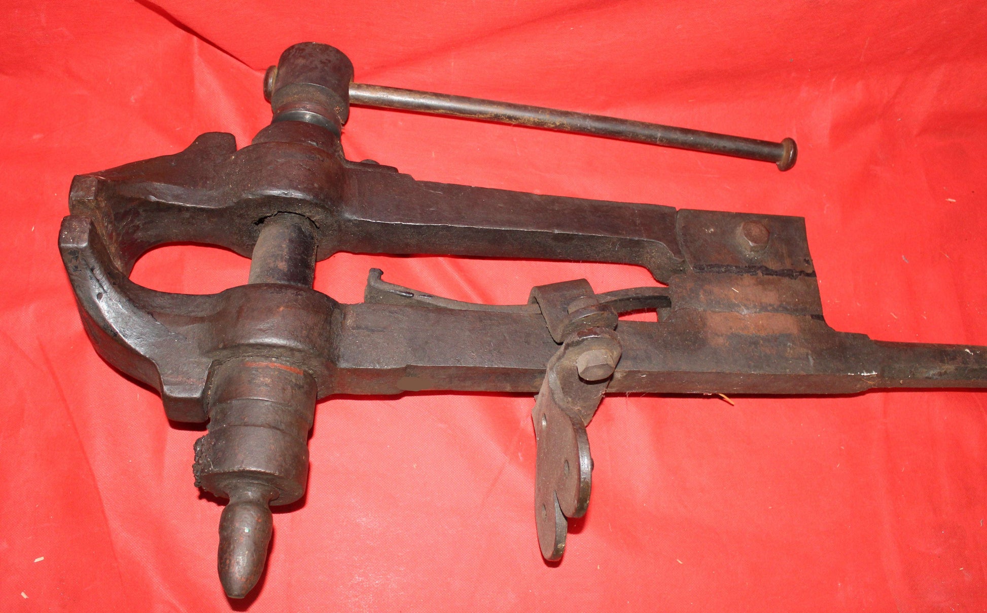 Tornillo de herrero en acero de fundición antiguo sobre fondo rojo, ideal para decoración de talleres o fraguas. Pieza robusta y funcional de colección.