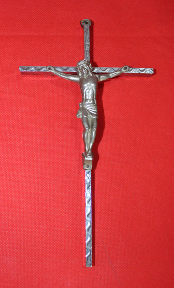 Crucificado de metal plateado sobre fondo rojo, diseño artesanal con detalles en relieve. Decoración religiosa de calidad y tradición cristiana.
