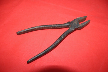 Alicate antiguo de hierro sobre fondo rojo, herramienta de colección de calidad ideal para decoración vintage en hogar o jardín.